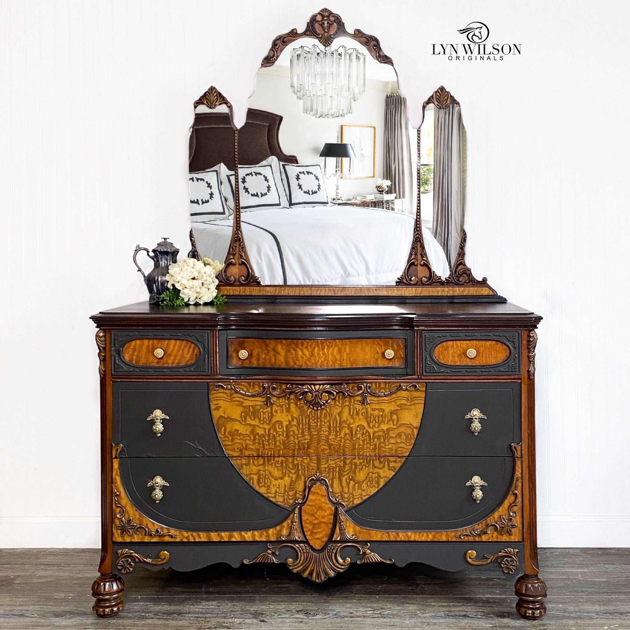 A vintage dresser with a tri-fold mirror refurbished by Lyn Wilson Originals has natural golden burlwood with Dixie Belle's Coffee Bean chalk mineral paint and bronze ornate accents.