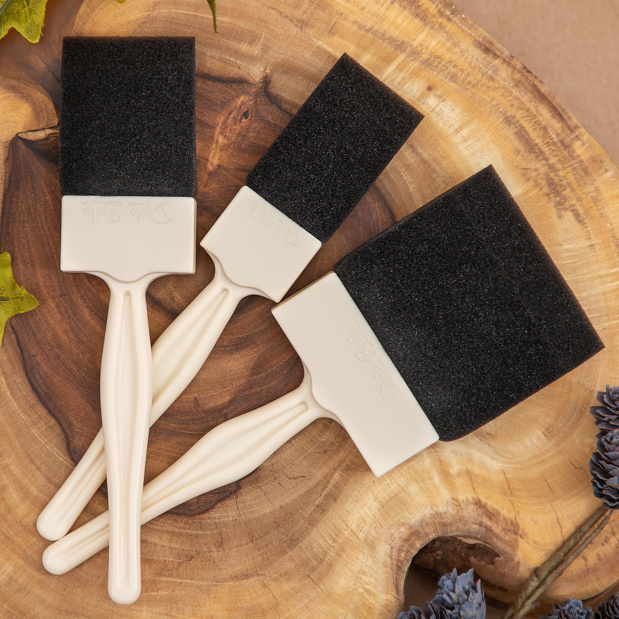 Three foam brushes in varying sizes are laying on a piece of wood.