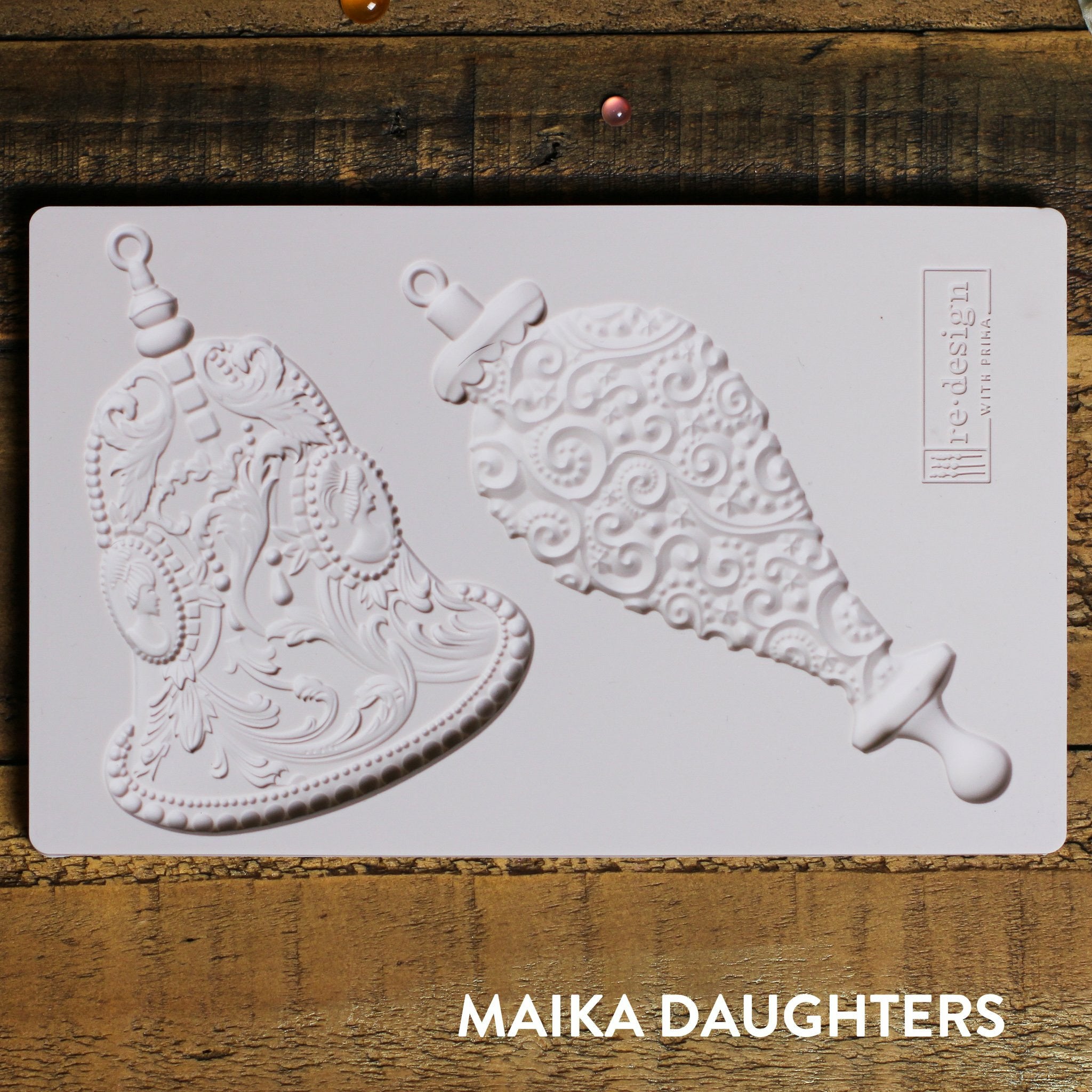 Wooden background with a mold of two bells and a redesign logo in the top right corner.  A white maika daughters logo is in the bottom right corner.