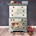 A tall chest dresser refurbished by Calle's ReDesigns is painted a diagonal ombre of light green to sage green and features ReDesign with Prima's Rustic Charm transfer on its 4 bottom drawers.