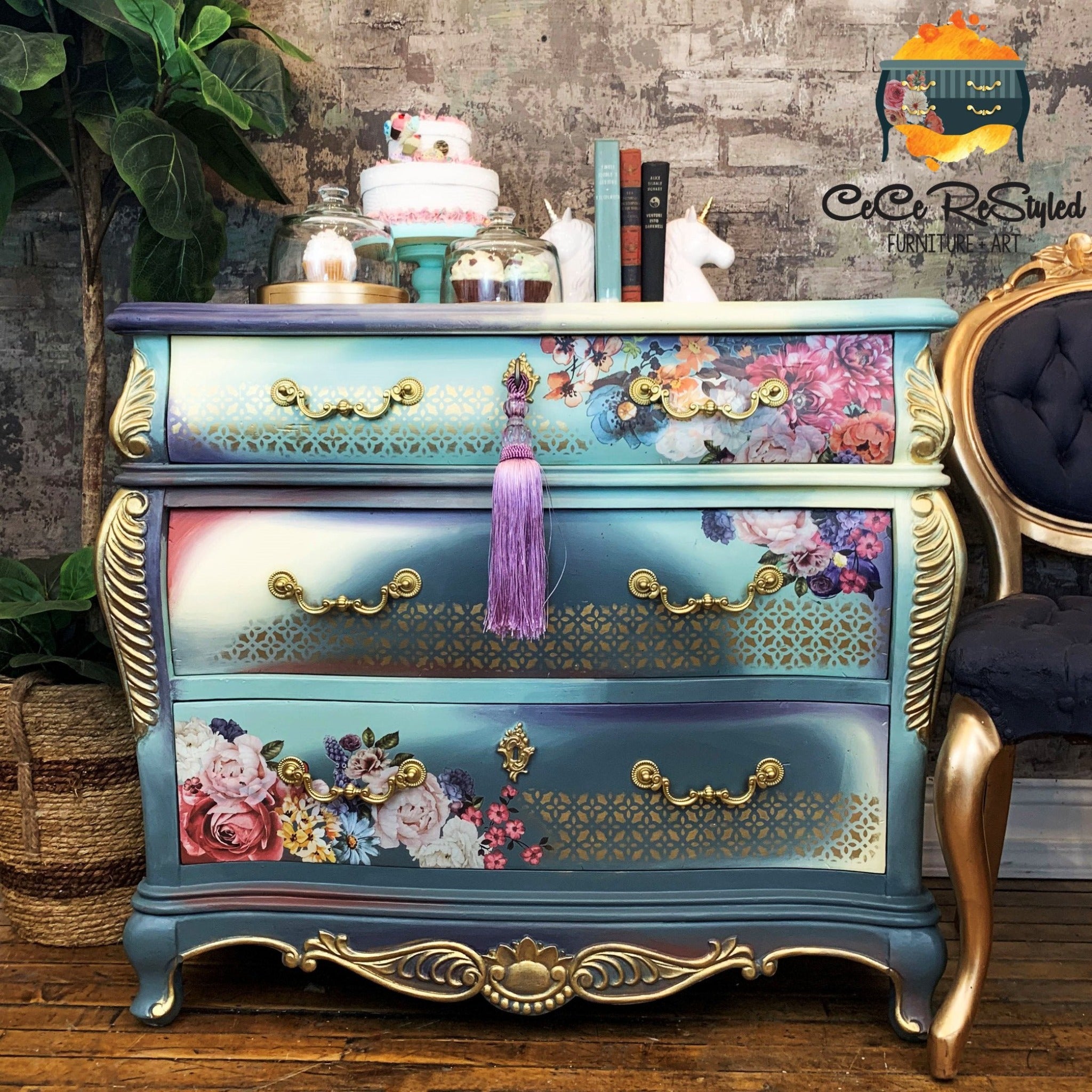 A vintage Bombay style dresser refurbished by CeCe ReStyled is painted a blend of blues and white with gold accents and features ReDesign with Prima's Ruby Rose rub-on transfer at the top right and bottom left of the top and bottom drawers.