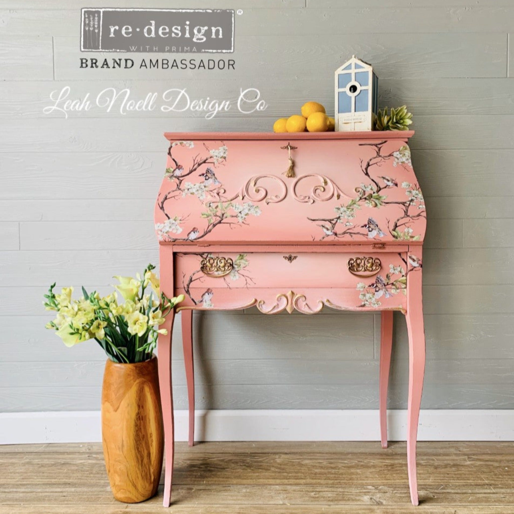 A vintage secretary's desk refurbished by Leah Noell Design Co. is painted light coral pink and features ReDesign with Prima's Blossom Flight transfer on it.
