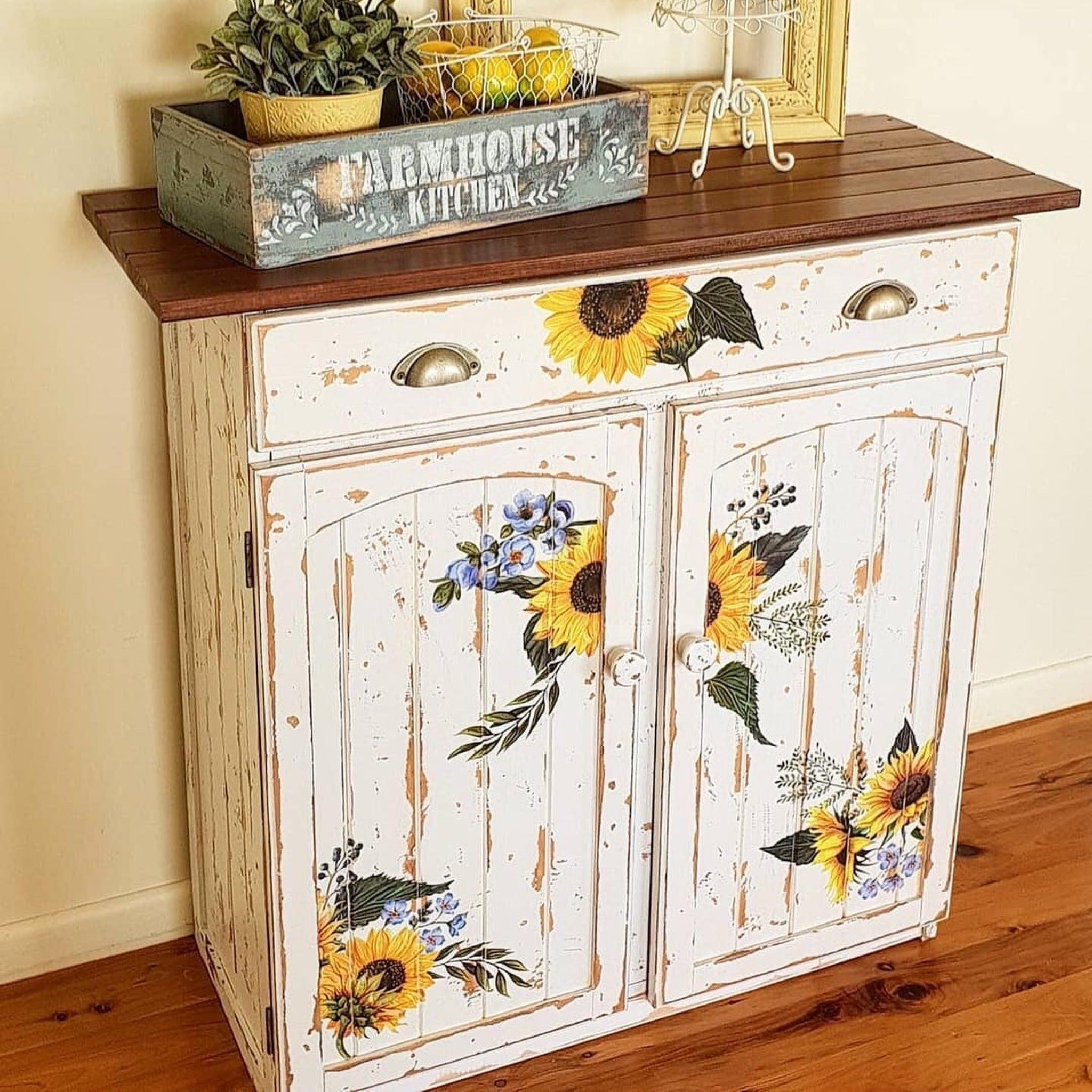 A vintage storage side table refurbished by Upcycled by Katie is painted distressed soft white and features ReDesign with Prima's Sunflower Fields transfer on its drawer and 2 doors.