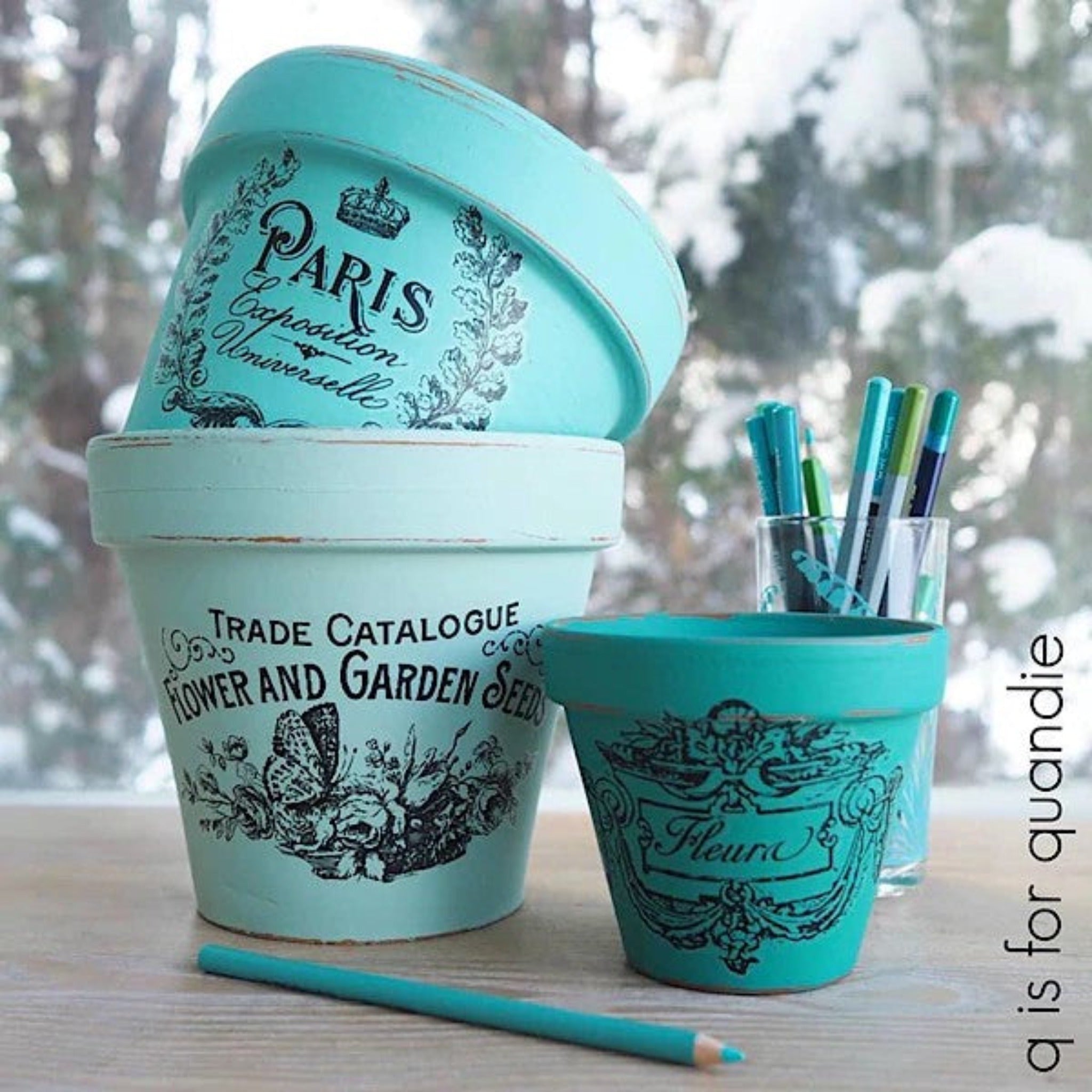 Three terra cotta clay pots refurbished by Q if for Quandie are painted teal and feature ReDesign with Prima's Classic Vintage Labels transfer on them.