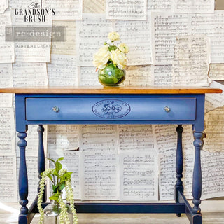 A vintage desk refurbished by The Grandson's Brush is painted blue with a natural wood top and feautres ReDesign with Prima's Classic Vintage Label transfers on its small drawer.