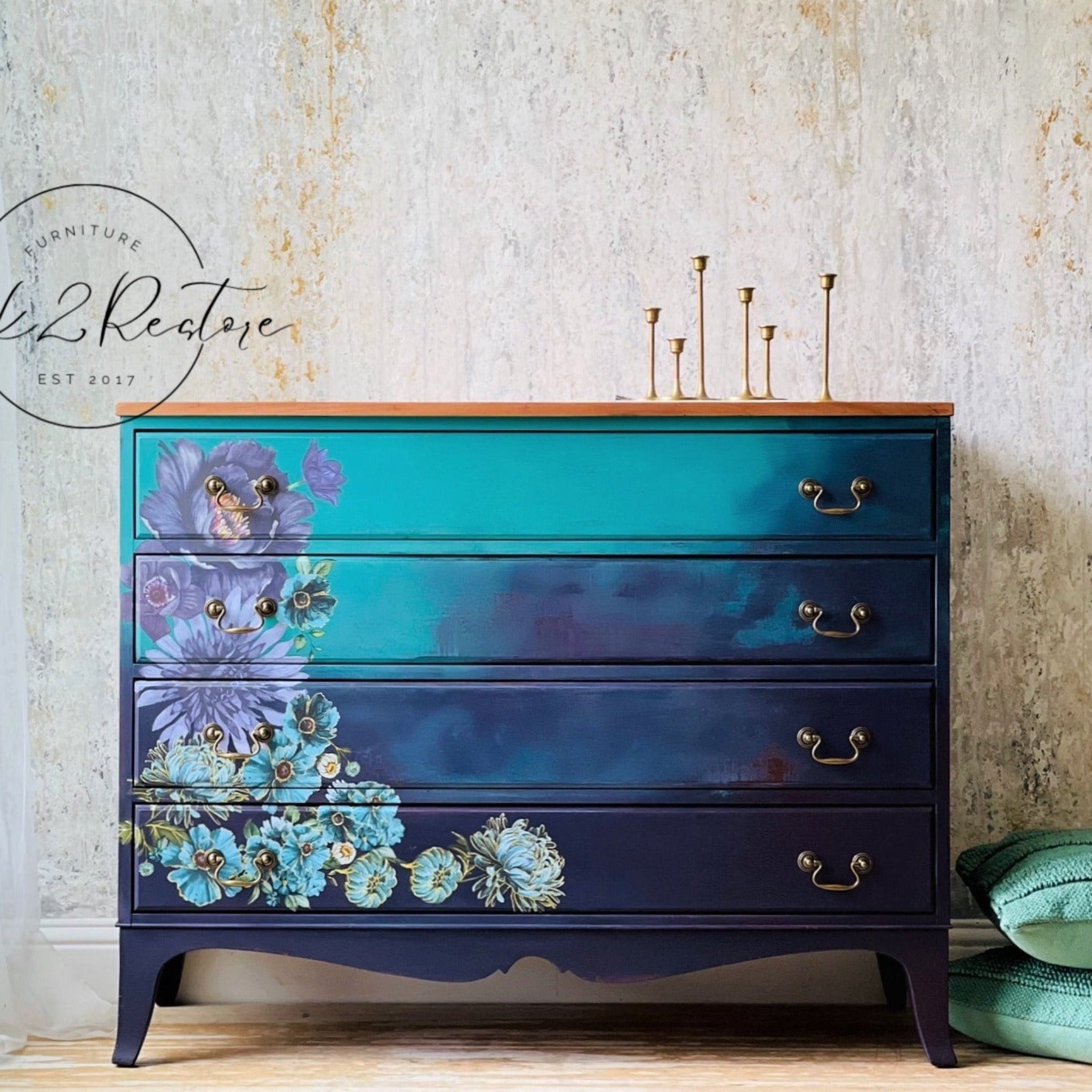 A 4-drawer dresser refurbished by Click 2 Restore is painted an ombre blend of bright teal down to navy blue and features ReDesign with Prima's Gilded Floral small transfer towards the bottom left corner of the dresser front.