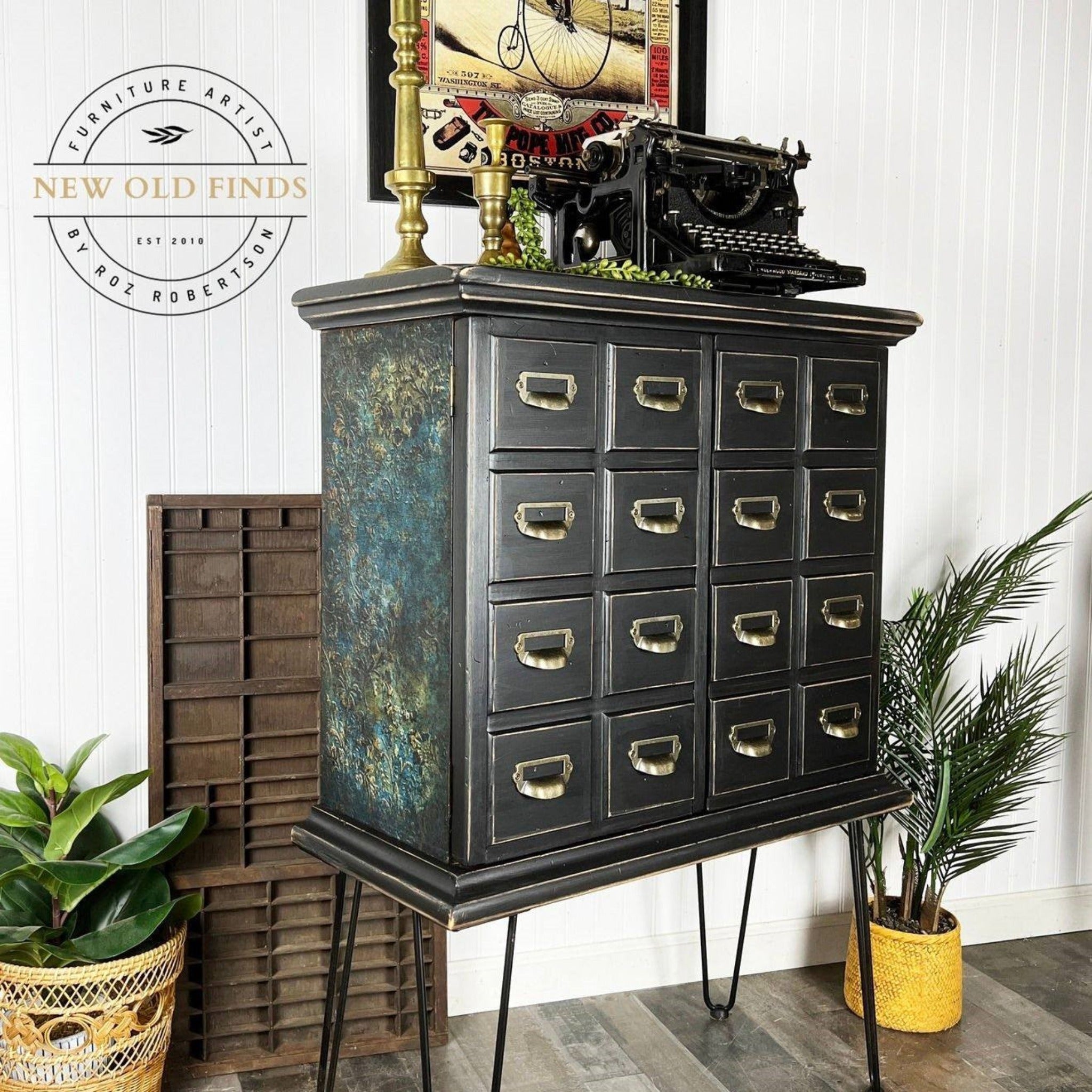 A vintage apothecary cabinet refurbished by New Old Finds is painted black and features ReDesign with Prima's Aged Patina A1 fiber paper on the sides.