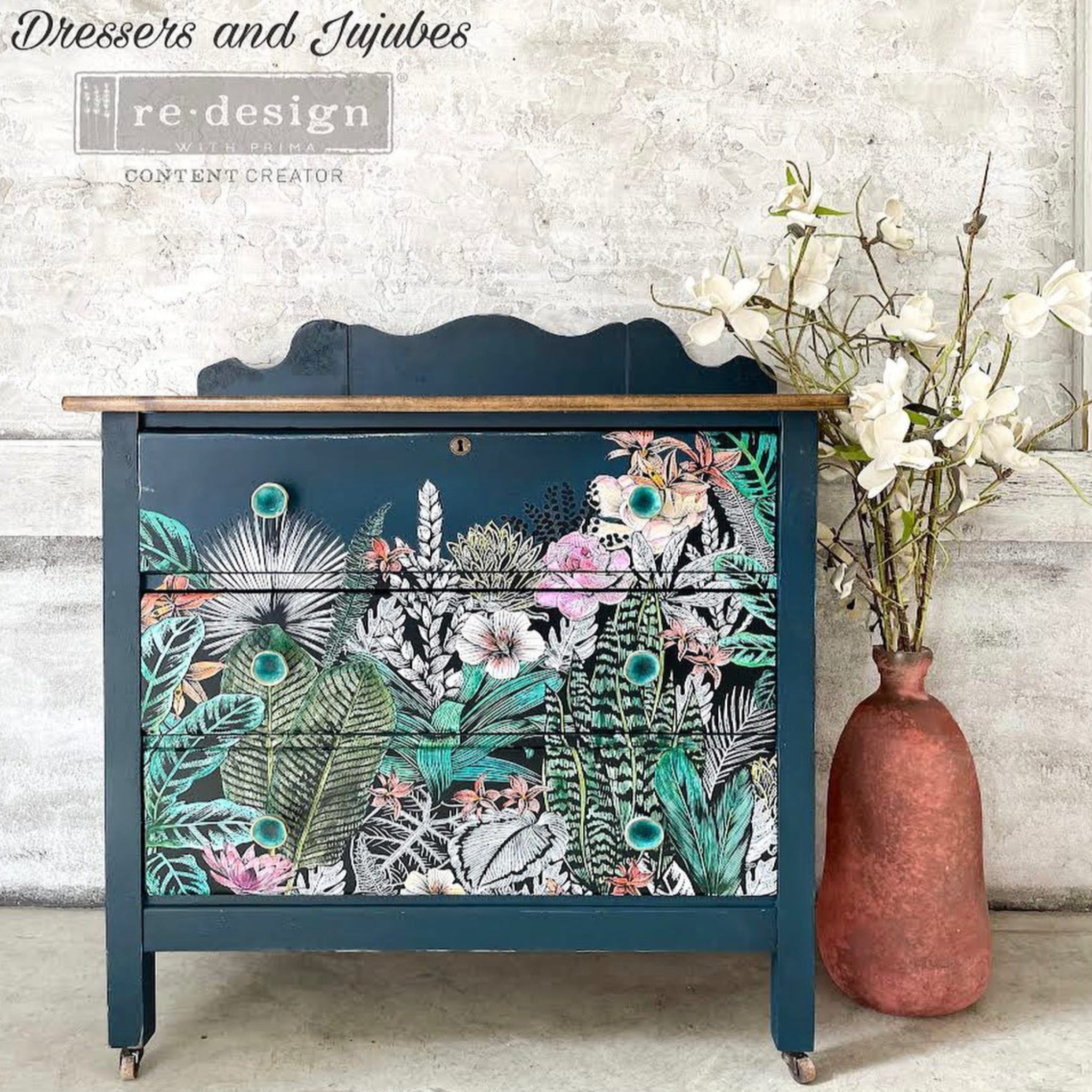 A vintage dresser refurbished by Dressers & Jujubes is painted blue and features a hand-painted colorful version of ReDesign with Prima's Abstract Jungle transfer on its 3 drawers.