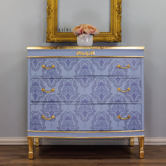 A dresser refurbished by Kacha is painted light blue with gold accents and features the Kacha Dana Damask transfer on its drawers.