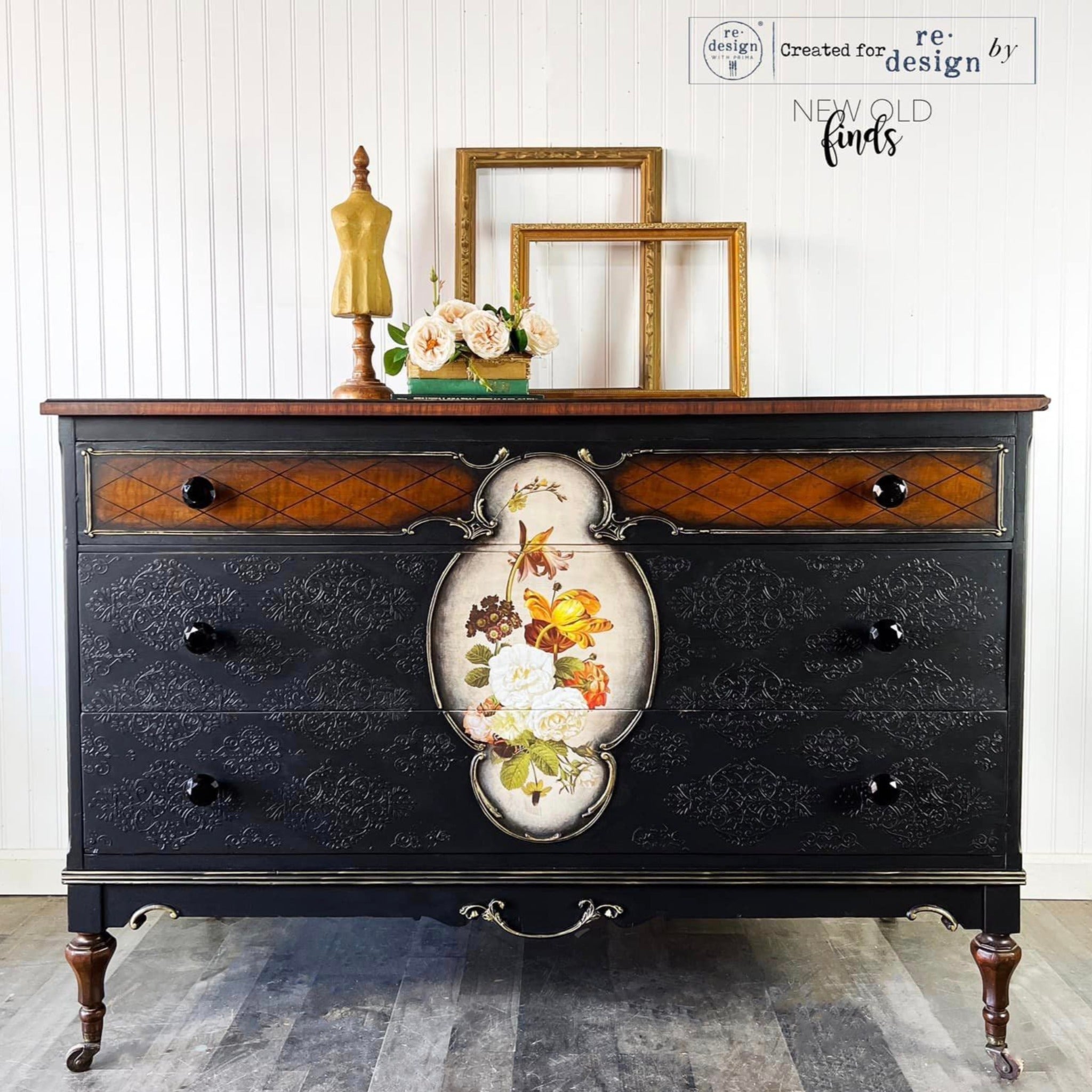 A large vintage dresser refurbished by New Old Finds is painted black with natural wood accents and features ReDesign with Prima's Blossomed Beauties small transfer inside a center frame against a light beige background on the front center of the dresser.