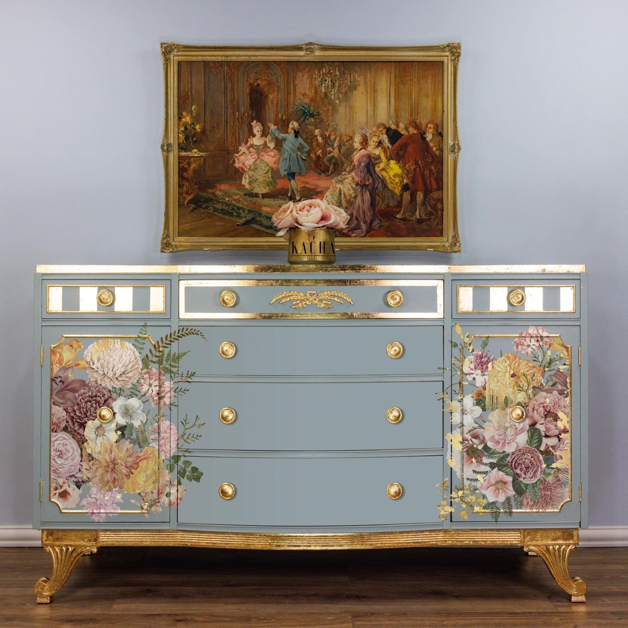 A vintage dresser refurbished by Kacha is painted pale sky blue with gold accents and features ReDesign with Prima's Kacha Woodland Floral transfer on its left and right doors.