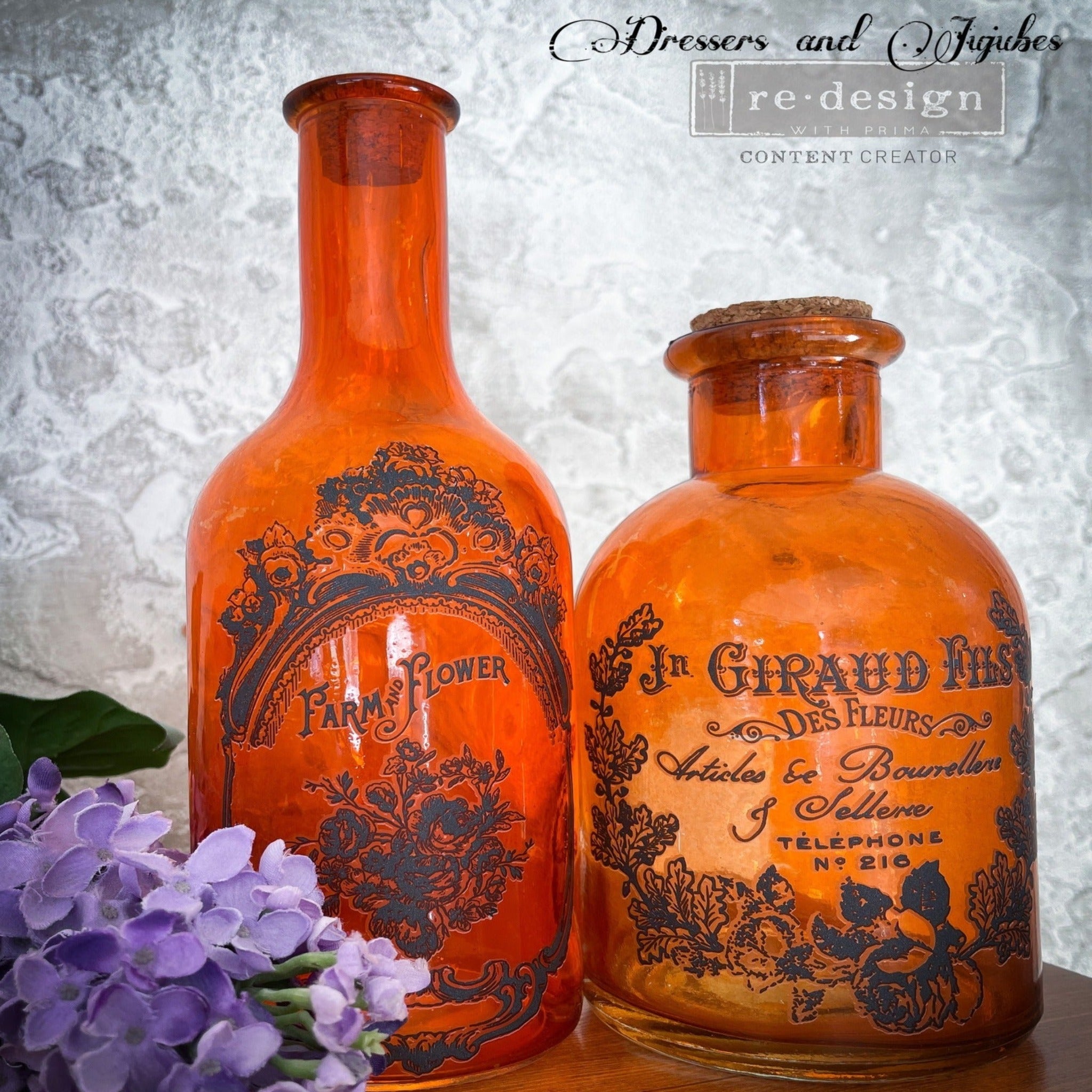 Two orange glass bottles with cork stoppers in them have been Refurbished by Dressers and Jujubes and feature ReDesign with Prima's French Labels small transfer on them.