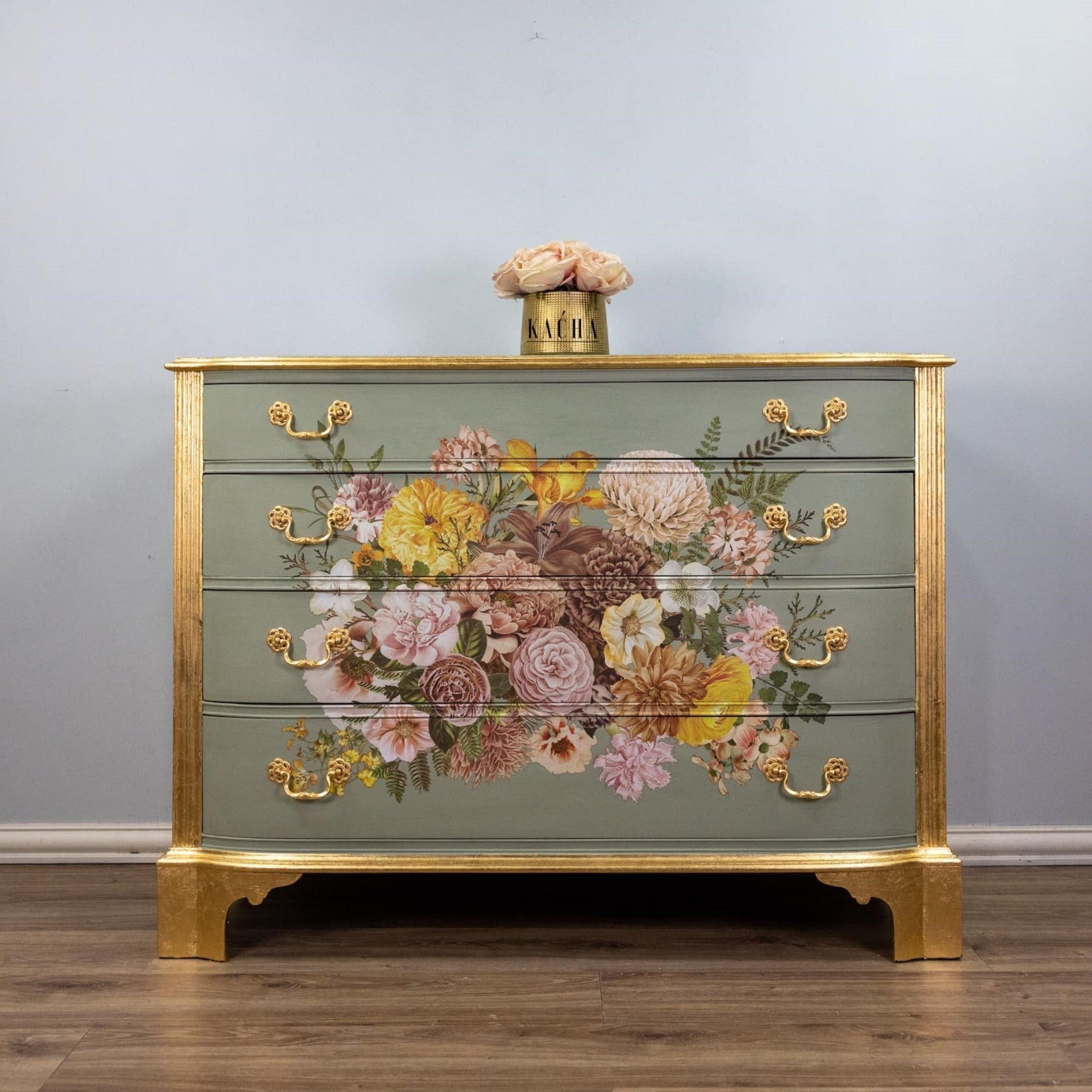 A vintage dresser refurbished by Kacha is painted a soft sage green with gold accents and features ReDesign with Prima's Kacha Woodland Floral transfer in the center of its 4 drawers.