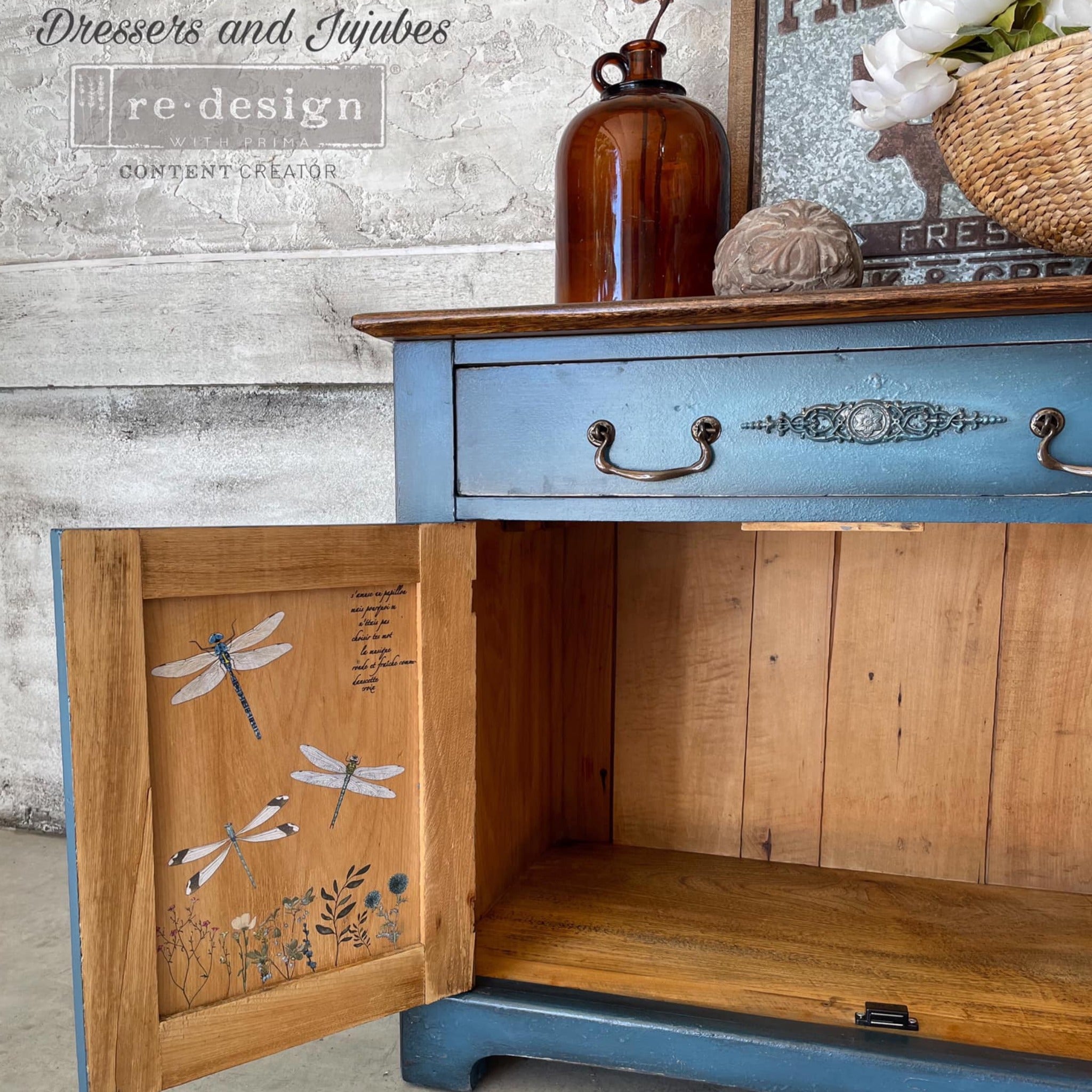 A small buffet table refurbished by Dresser and Jujubes is painted a blend of blues and features ReDesign with Prima's Spring Dragonfly small transfer on the inside of its 2 doors.
