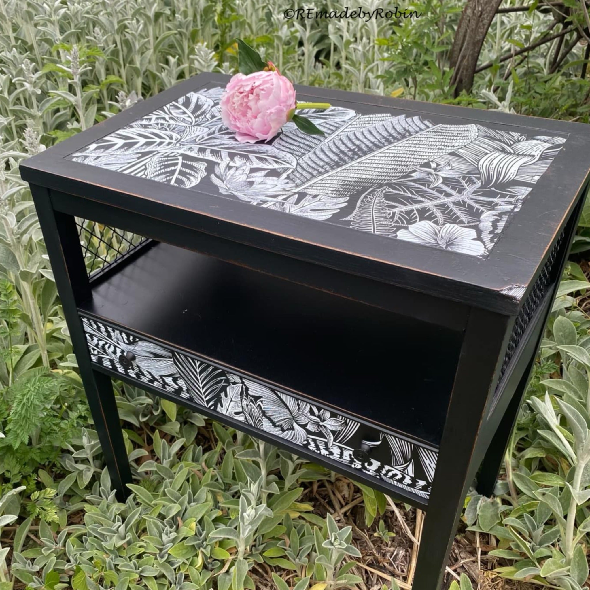 A vintage nightstand refurbished by ReMade by Robin is painted black and features ReDesign with Prima's Abstract Jungle on the top and fron small drawer beneath an open shelf.