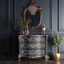A vintage 4-drawer desk is painted dark grey with gold accents and features ReDesign with Prima's Albery transfer on its drawers. A large ornate mirror framed in gold is above the dresser.