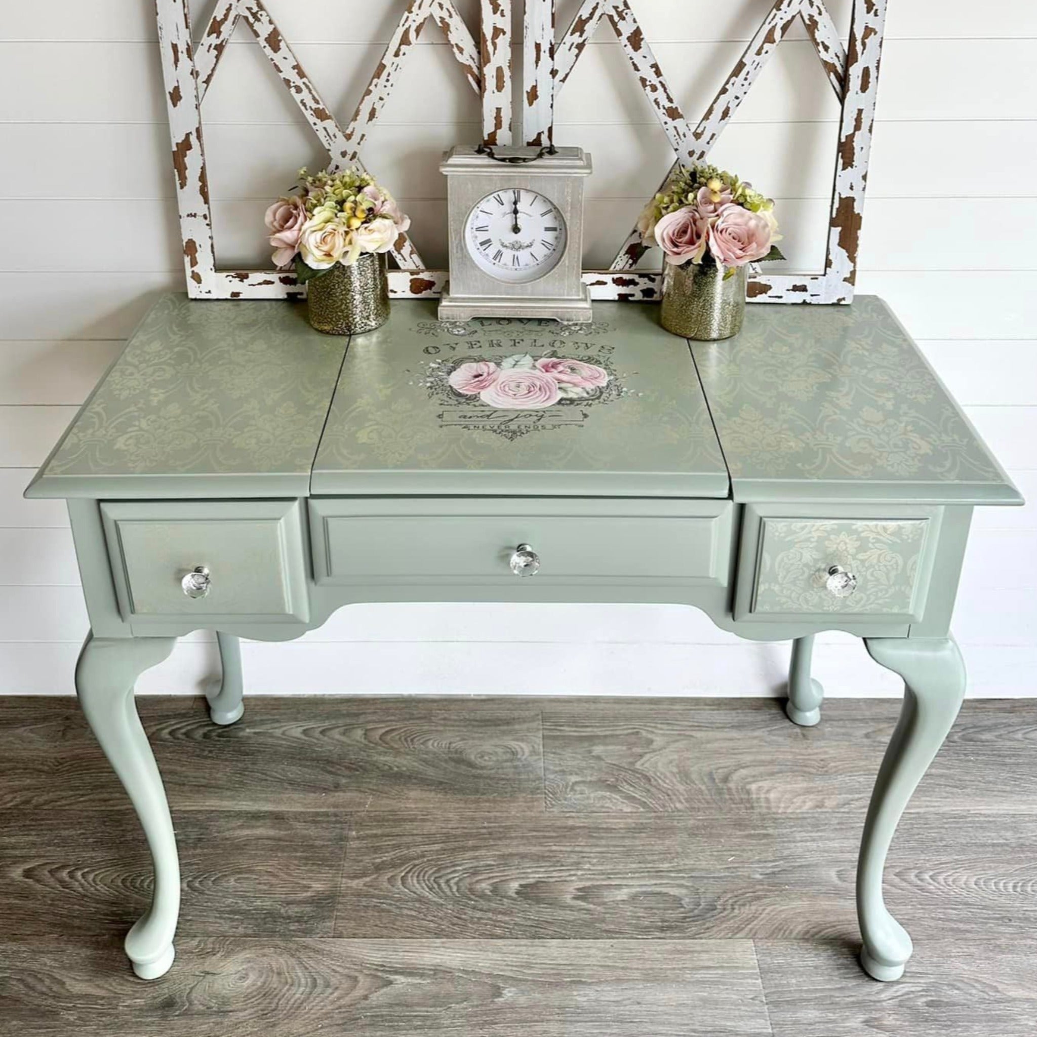 A vintage vanity desk refurbished by The Shabby Pearl is painted light sage green and features ReDesign with Prima's Overflowing Love transfer in the middle of the desktop on a lift-up lid.