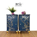 Two vintage nightstands with storage refurbished by Myriad Interiors are painted deep navy blue with gold French Provencial legs and features ReDesign with Prima's Kacha A Bird Song Gold Foil transfer on the front of them.