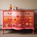 A vintage 3-drawer dresser is painted a blend of coral pinks and features ReDesign with Prima's Poppy Gardens transfers on its bottom 2 drawers.