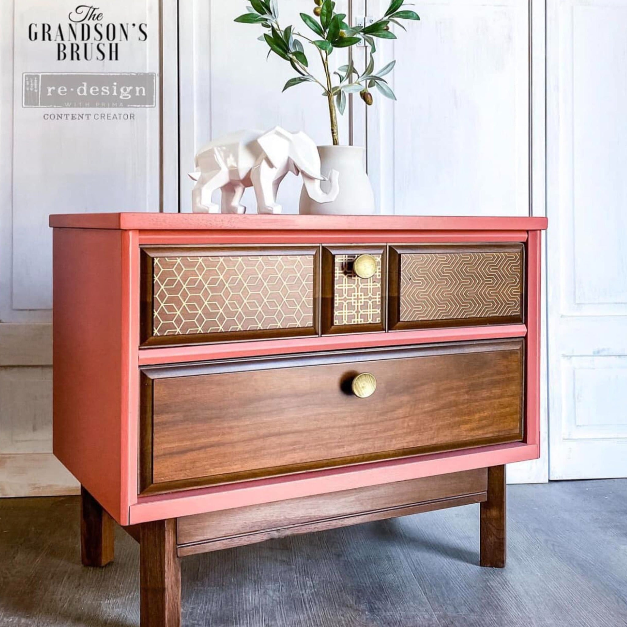 A 2-drawer end table refurbished by The Grandson's Brush is painted coral pink with natural wood drawers and features ReDesign with Prima's Motif Geometrique small transfers on its top drawer inlays.