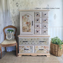 A vintage armoire refurbished by Lubbly Jubbly Furniture is painted light beige and features ReDesign with Prima's Enchanted Romance tissue paper on its door inlay and many drawers.