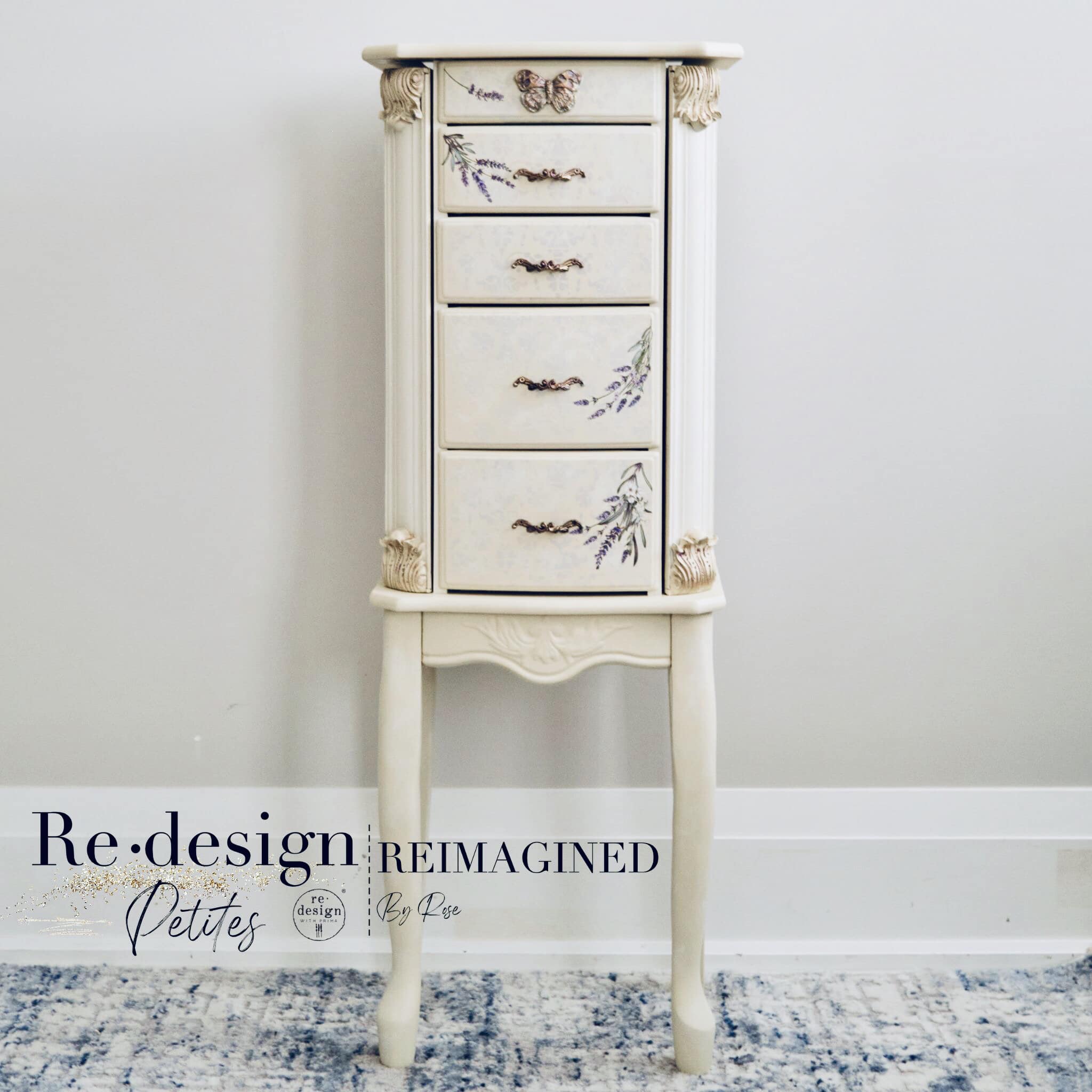 A standing vintage jewelry armoire refurbished by Reimagined by Rose is painted ivory white and features ReDesign with Prima's Lavender Bunch small transfer on 4 of the 5 drawers.