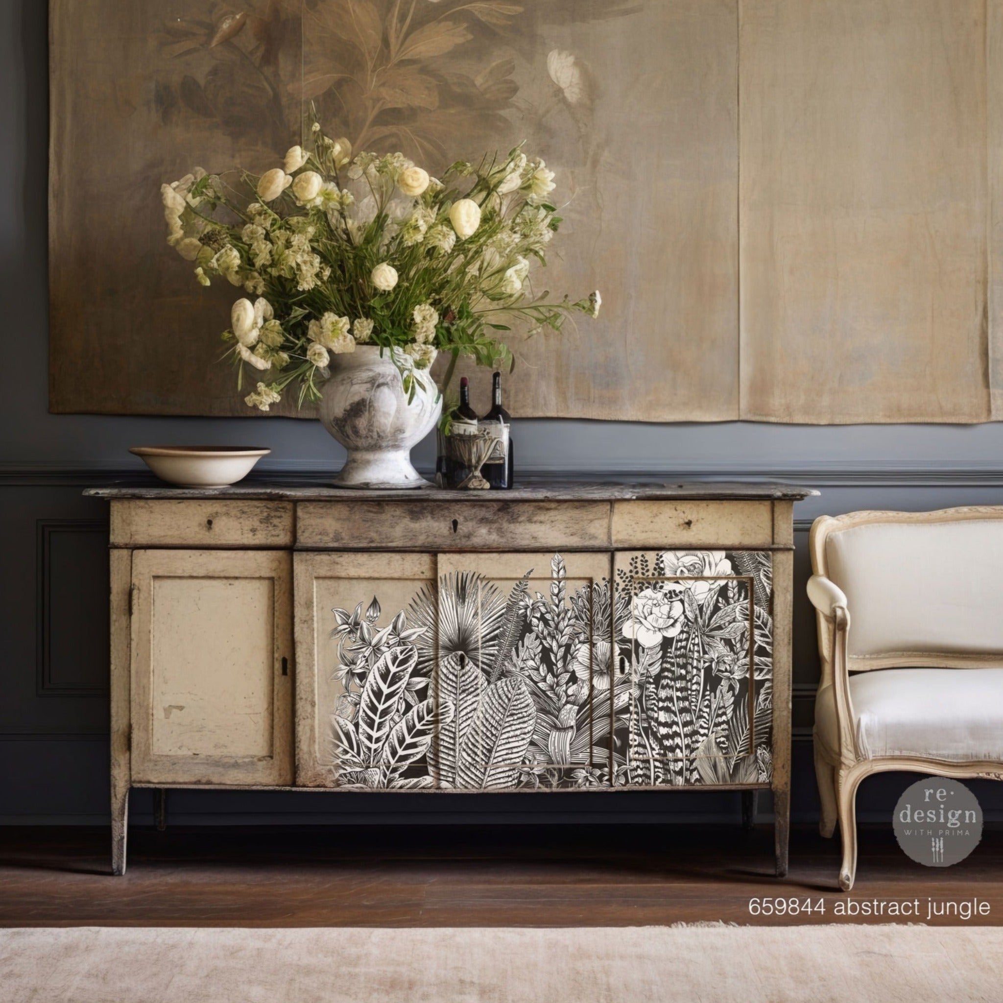A vintage console table is light beige with distressing and features ReDesign with Prima's Abstract Jungle transfer on 3 of its 4 storage doors.