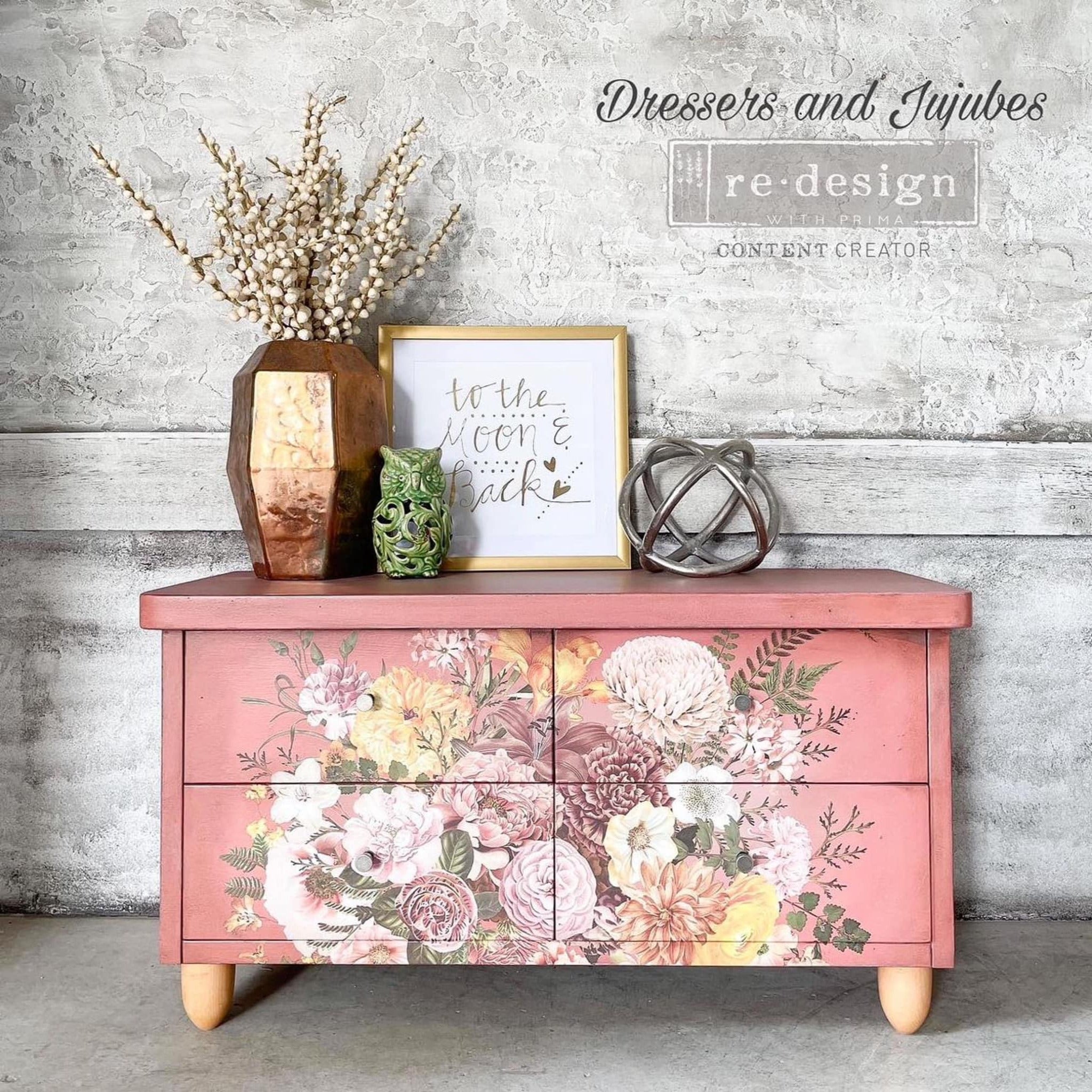 A vintage 4-drawer dresser refurbished by Dressers and Jujubes is painted coral pink and features ReDesign with Prima's Kacha Woodland Floral transfer on the center of its drawers.