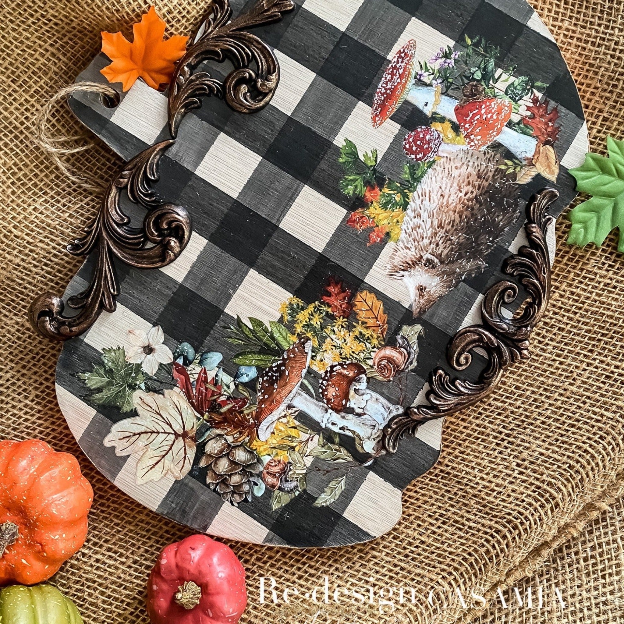 A wood pumpkin craft project created by CasaMia is painted black and white plaid and features ReDesign with Prima's Autumn Essentials small transfer on it along with some bronze colored scroll silicone mould castings.