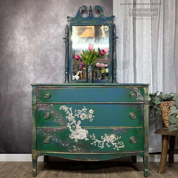 A vintage 3-drawer dresser with an attached mirror refurbished by Laura Designs Shop is painted a blend of blue and green and features ReDesign with Prima's Alaina Toile transfer on its bottom 2 drawers.