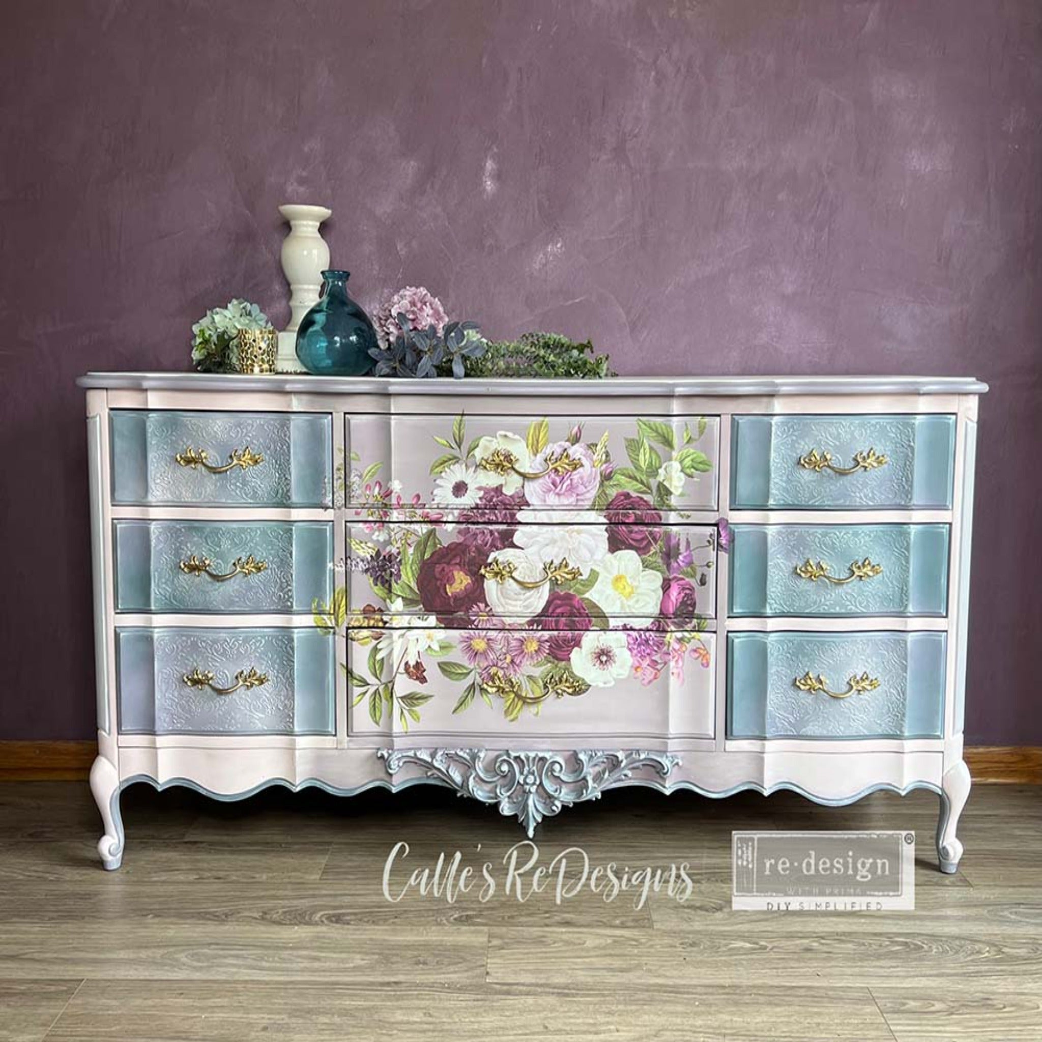 A vintage large 9 drawer dresser refurbished by Calle's ReDesigns is painted light beige and features ReDesign with Prima's Kacha Morning Purple transfer on its 3 center drawers. The 6 drawers on the left and right side are painted light sky blue.