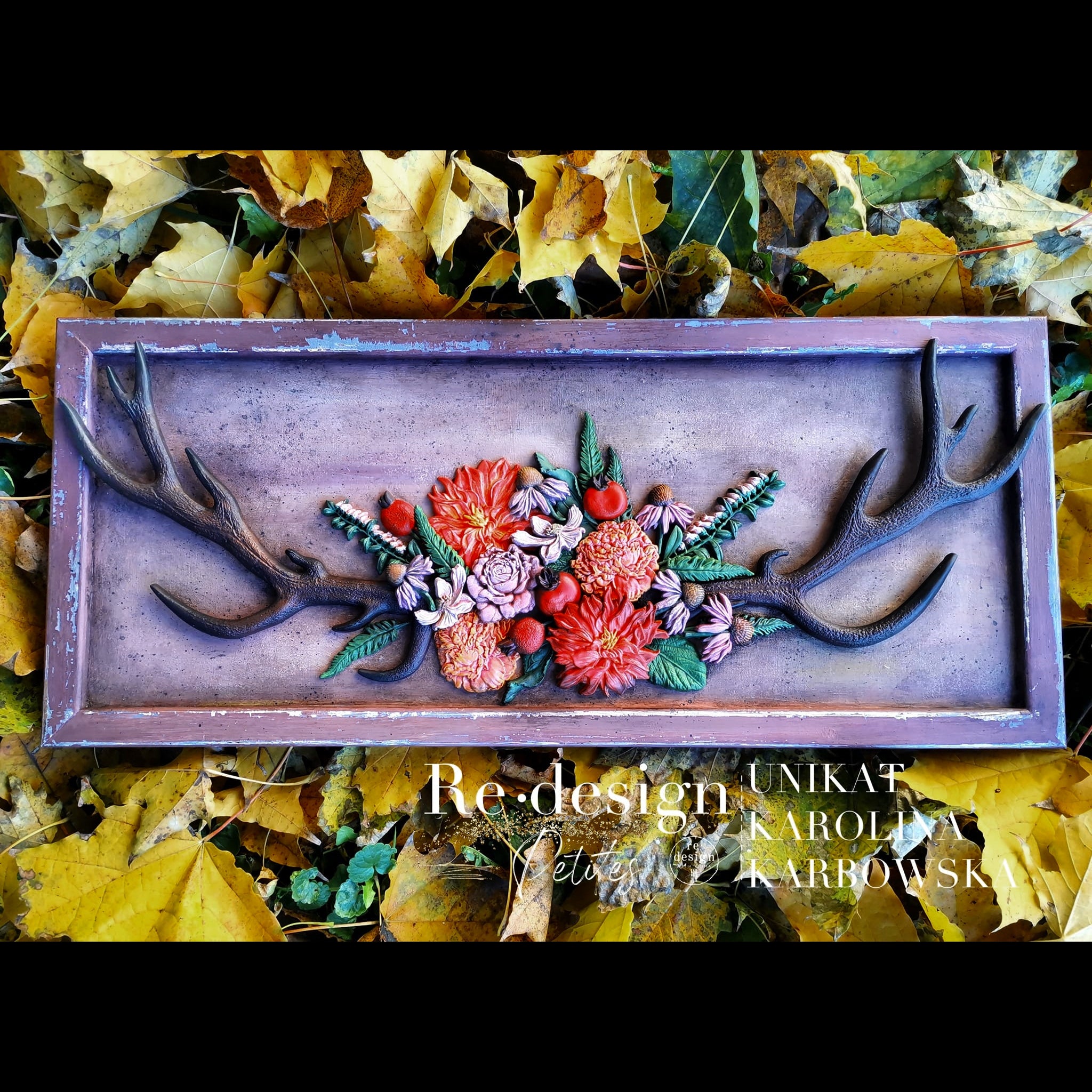 A rectangular wood frame created by Unikat Karolina Karbowska features ReDesign with Prima's Logger's Lodge silicone moulds on it. The antlers are painted dark brown and the flowers are colorfully painted. Black borders are on the top and bottom of the photo.