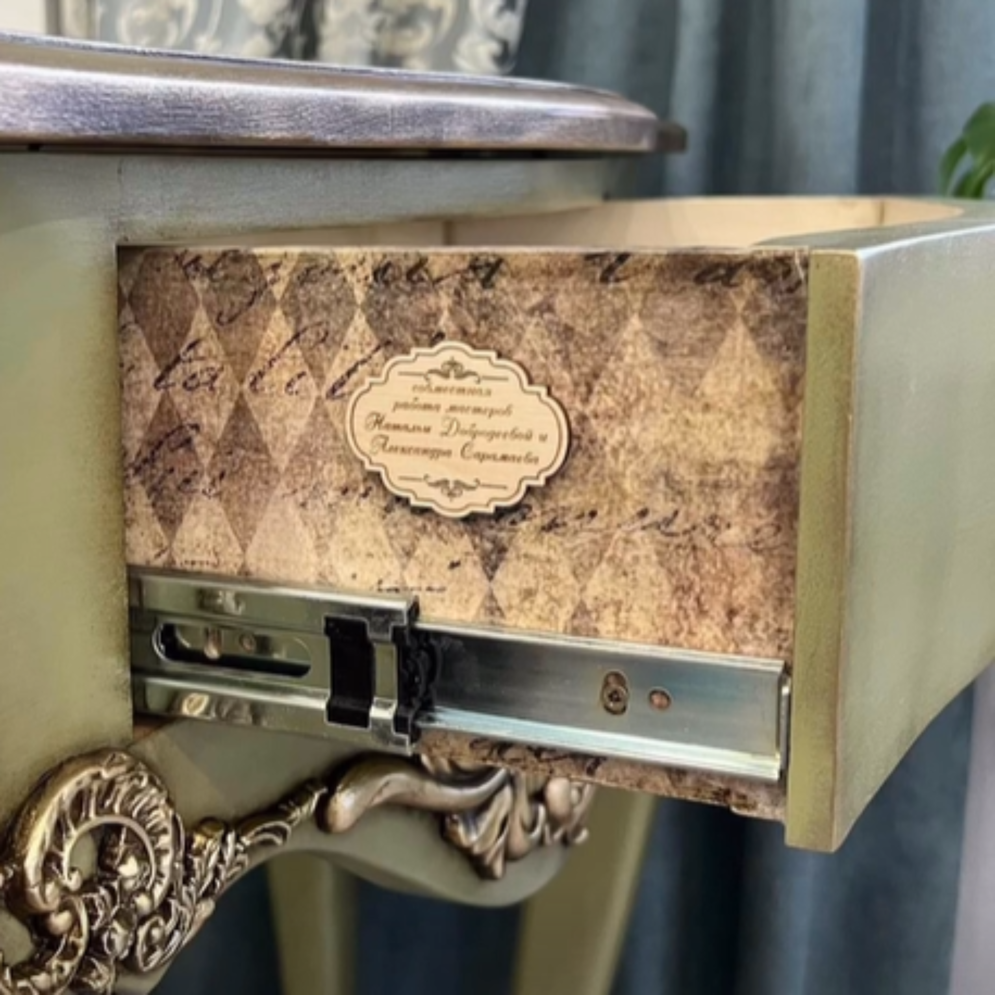 A close-up view of a vintage small desk refurbished by @provans_volga on Instagram is painted olive green and features Decoupage Queen's Neutral Harlequin rice paper on the sides of its 1 small drawer.