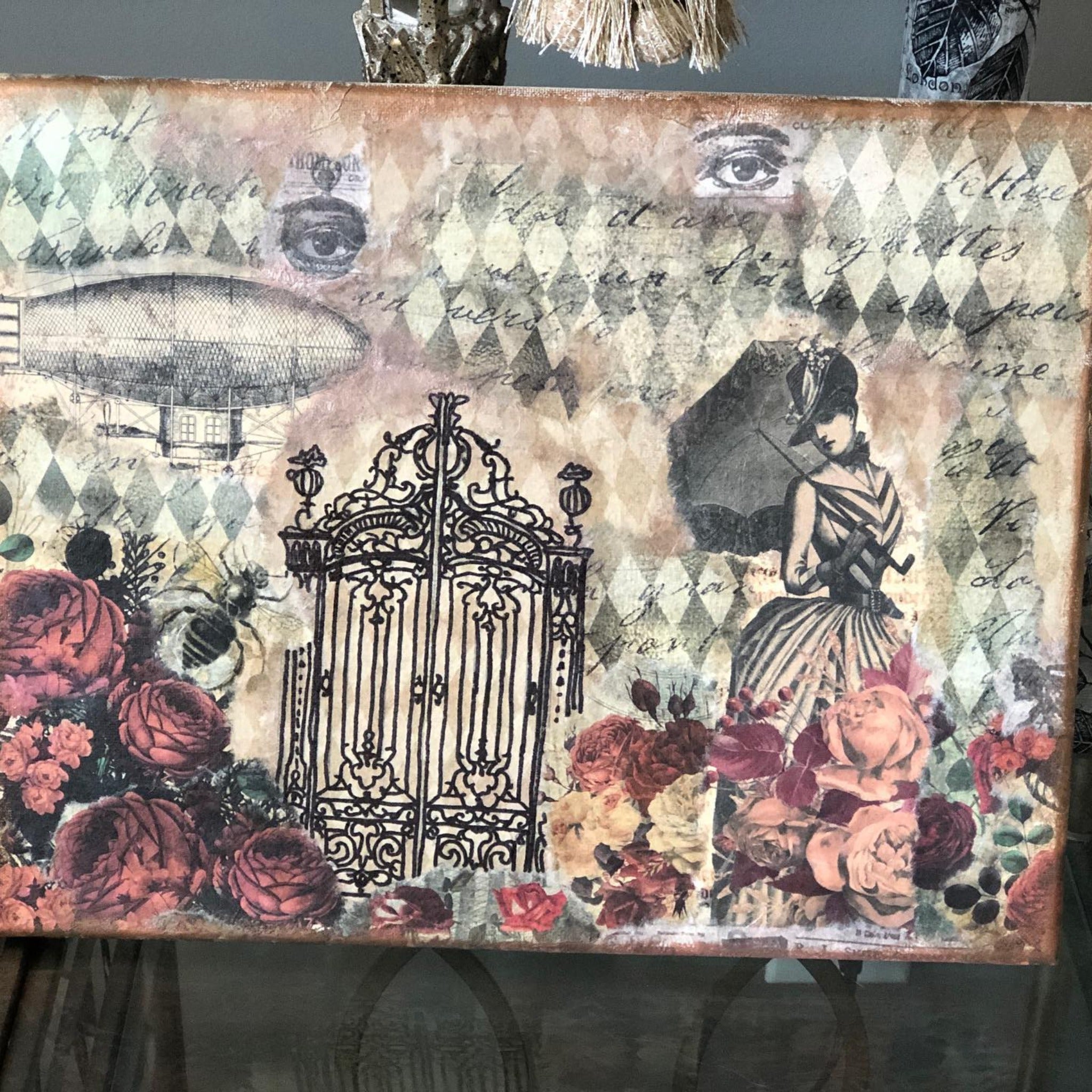 A large canvas features Decoupage Queen's Neutral Harlequin rice paper as a background. In the foreground are roses, an iron ornate gate, a Victorian woman, and a zeppelin airship.