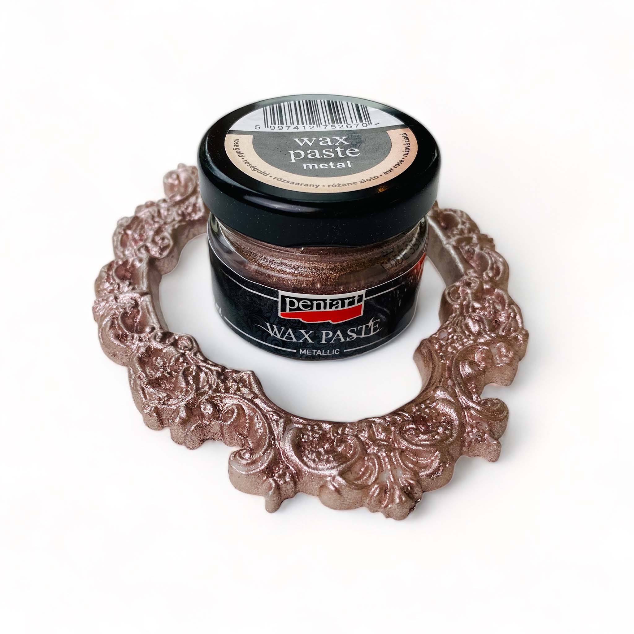 An open jar of a 20ml/0.68 ounce jar of metallic Rose Gold Wax Paste by Pentart is against a white background. An ornate frame covered with Rose Gold Pentart wax paste surrounds the jar.