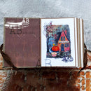 Open book with a painting of a house and pumpkin on a textured surface