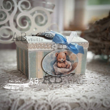 Decorative box with a teddy bear illustration and blue ribbon on a textured surface.
