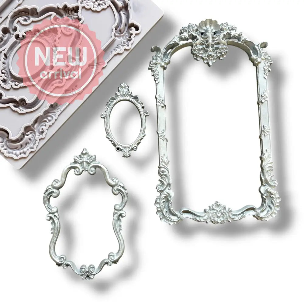 A light grey silicone mold and silver colored castings of 3 intricately detailed baroque flourish frames are against a white background.