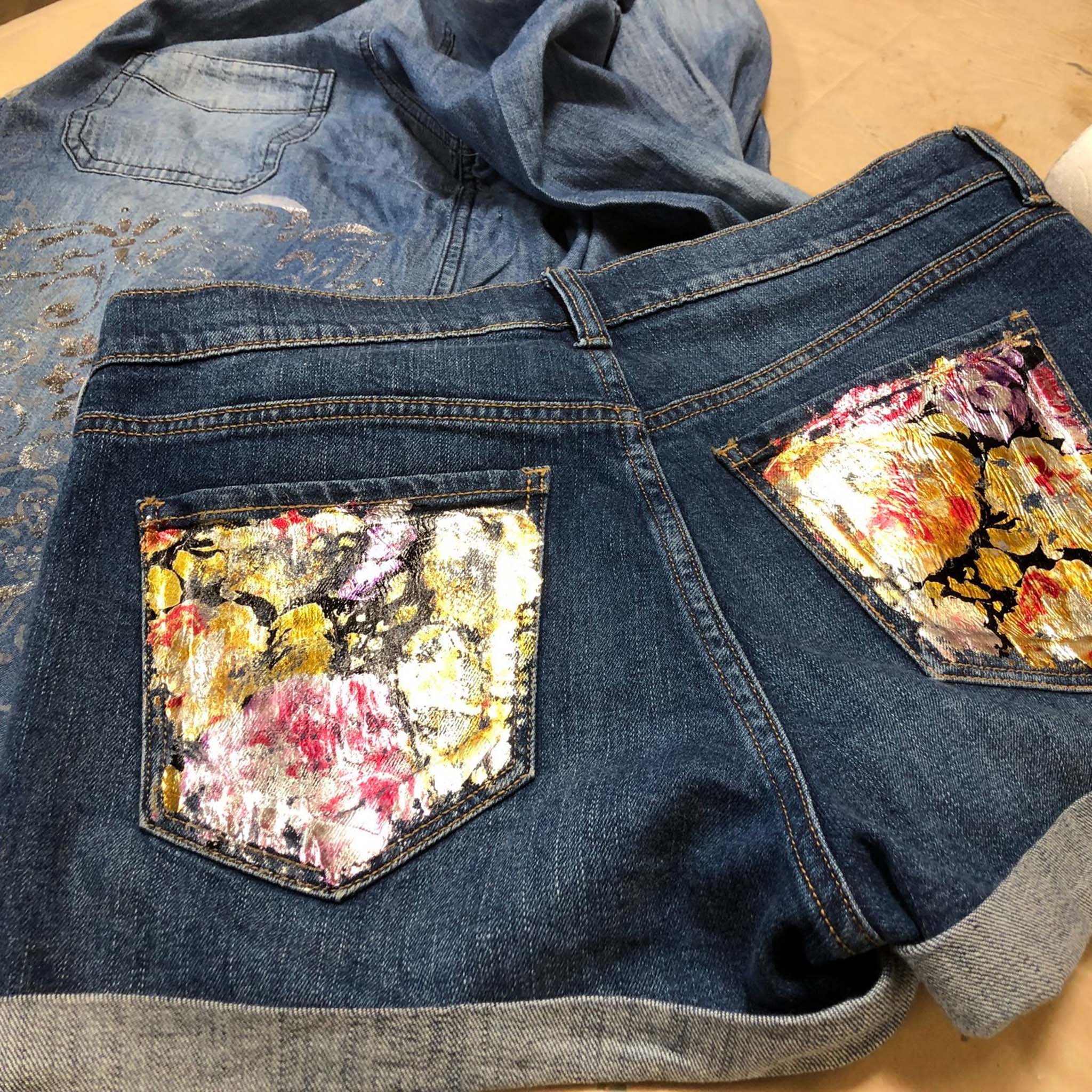 A pair of blue jean shorts features Artictic Painting Studio's Baylee Flowers metallic transfer foil on its back pockets.