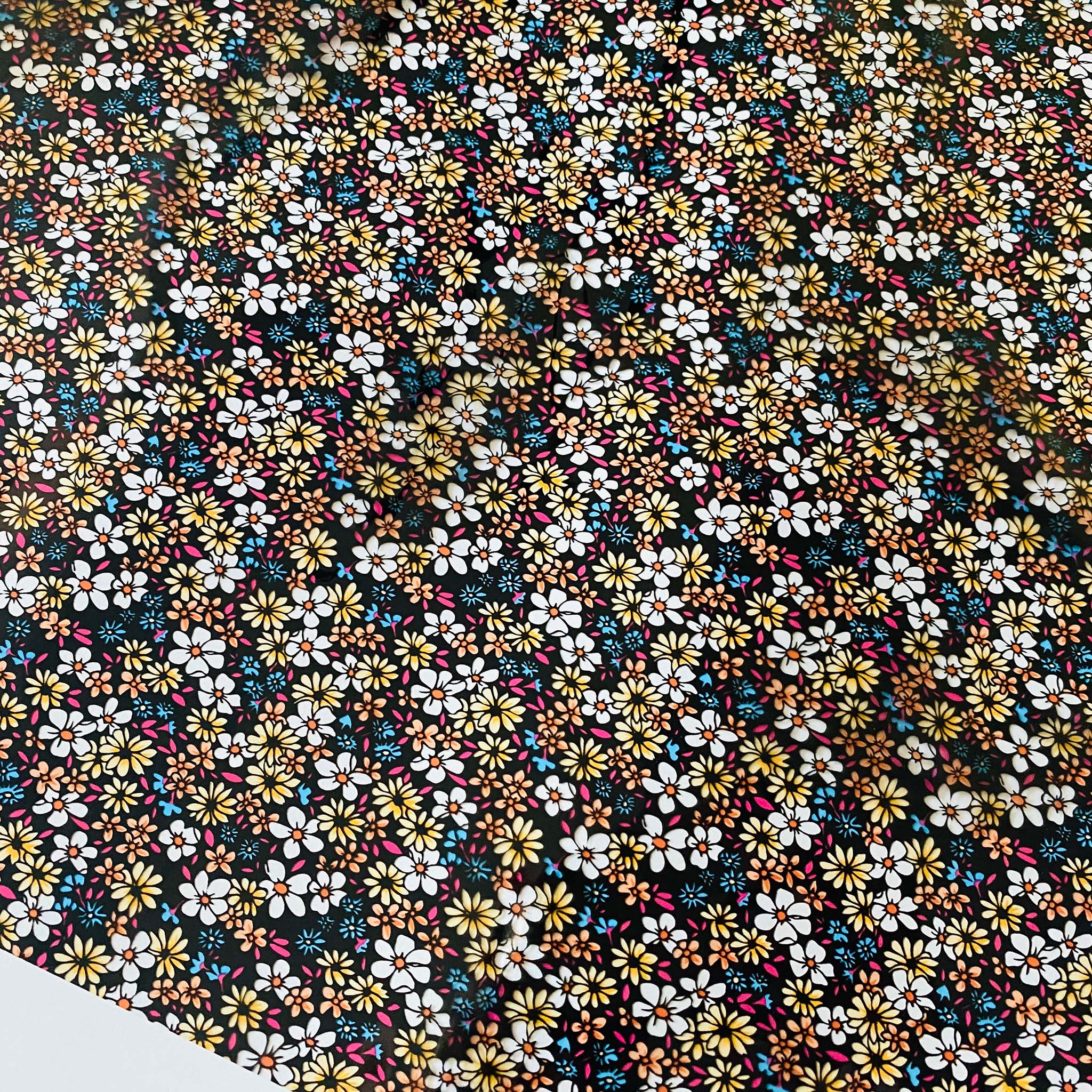 Close-up of a roll of a transparent metallic foil transfer that features an array of small flowers with a transparent black background is against a white background.