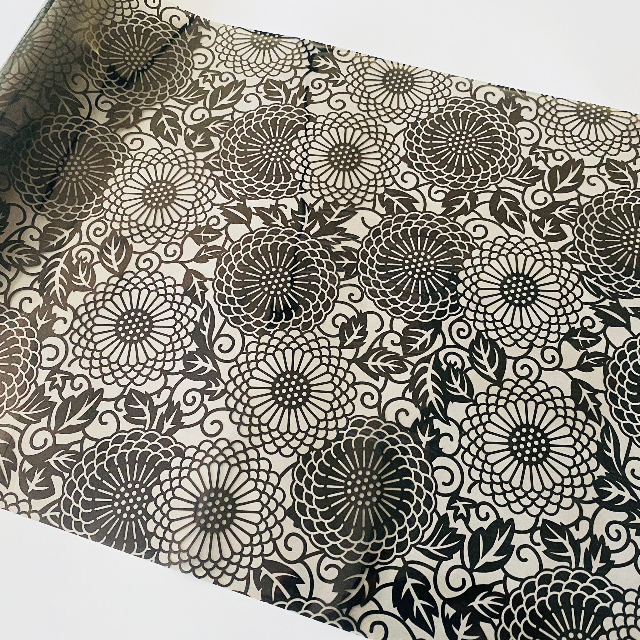 A roll of a foil transfer that features a black circular floral pattern is against a white background.