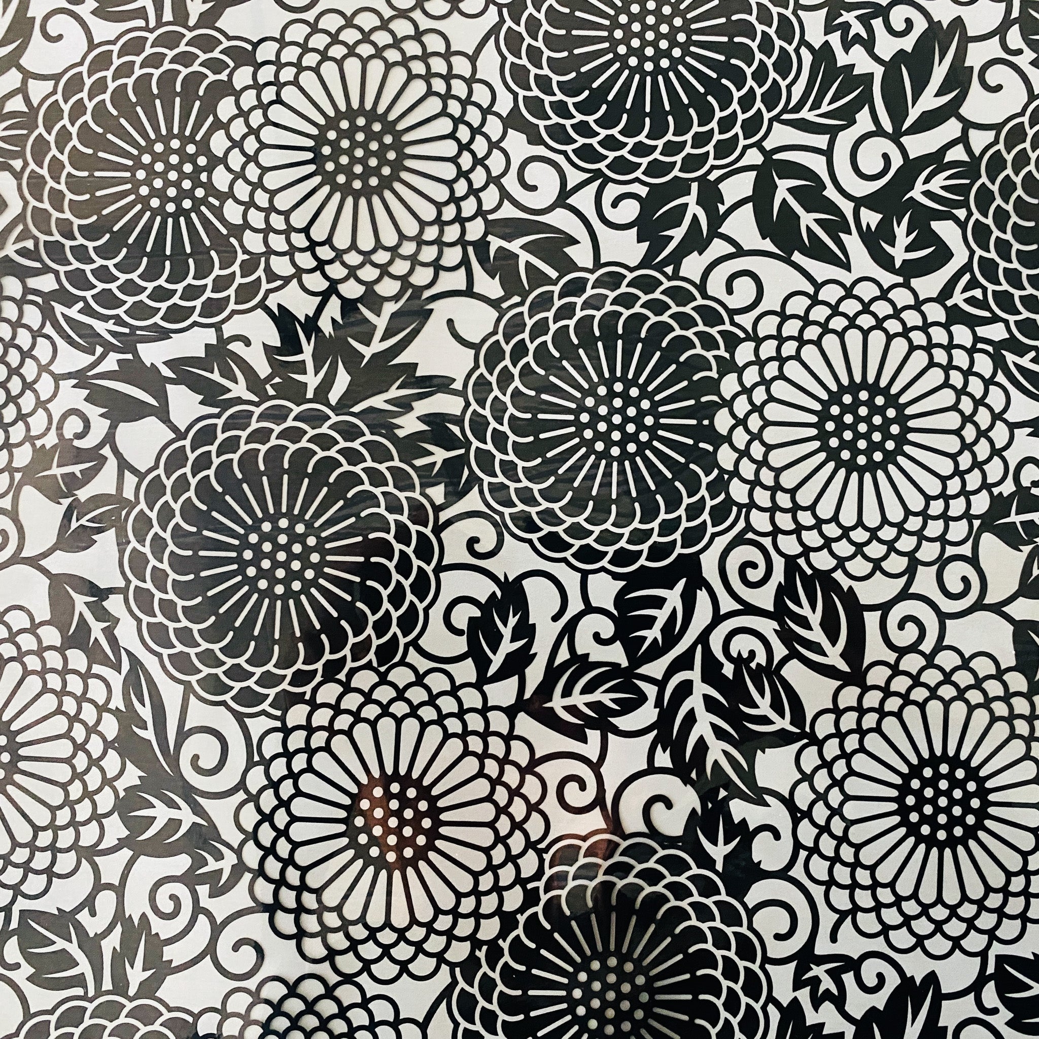 A close-up of a foil transfer that features a black circular floral pattern is against a white background.