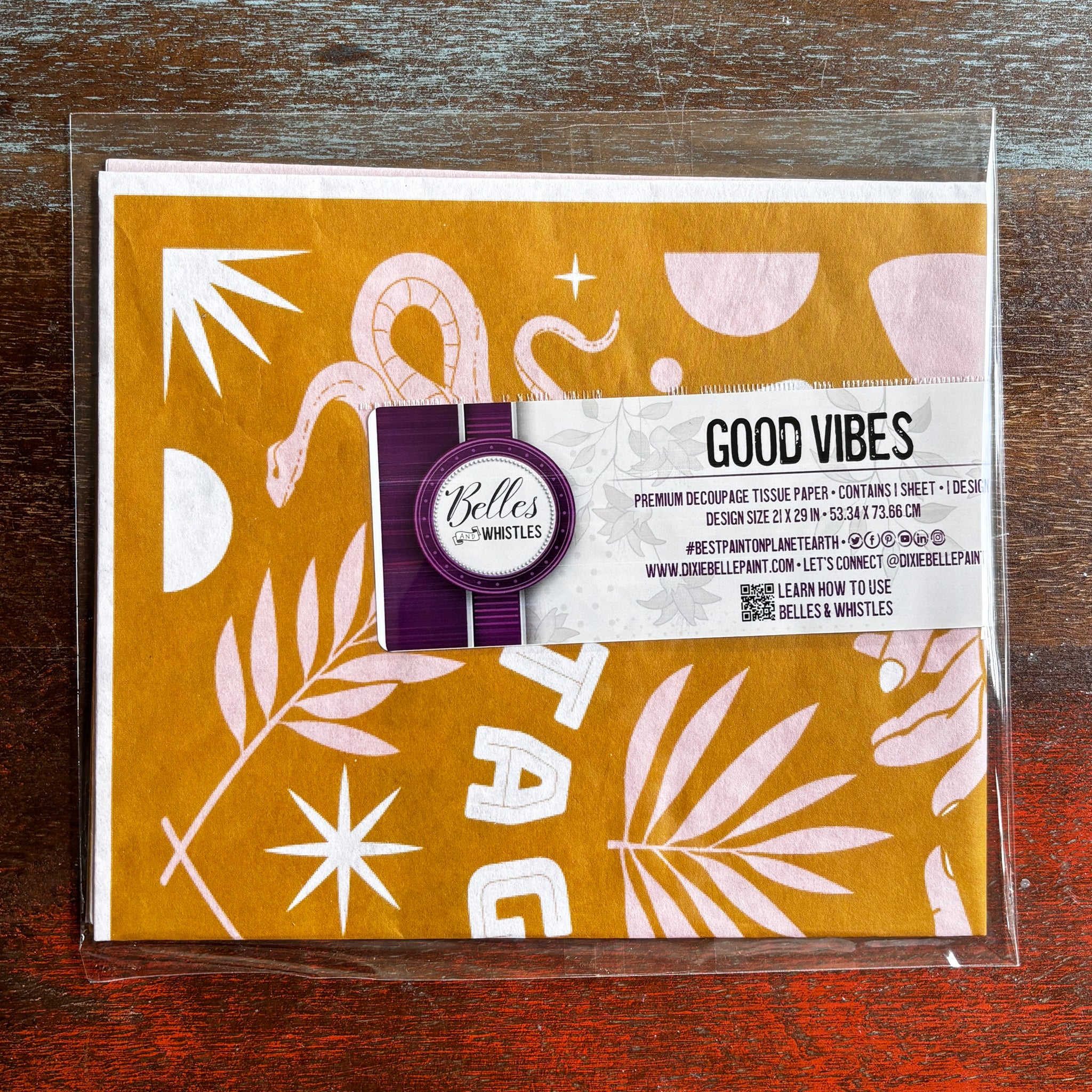 A package of Belles & Whistles' Good Vibes tissue paper is against a dark wood background.