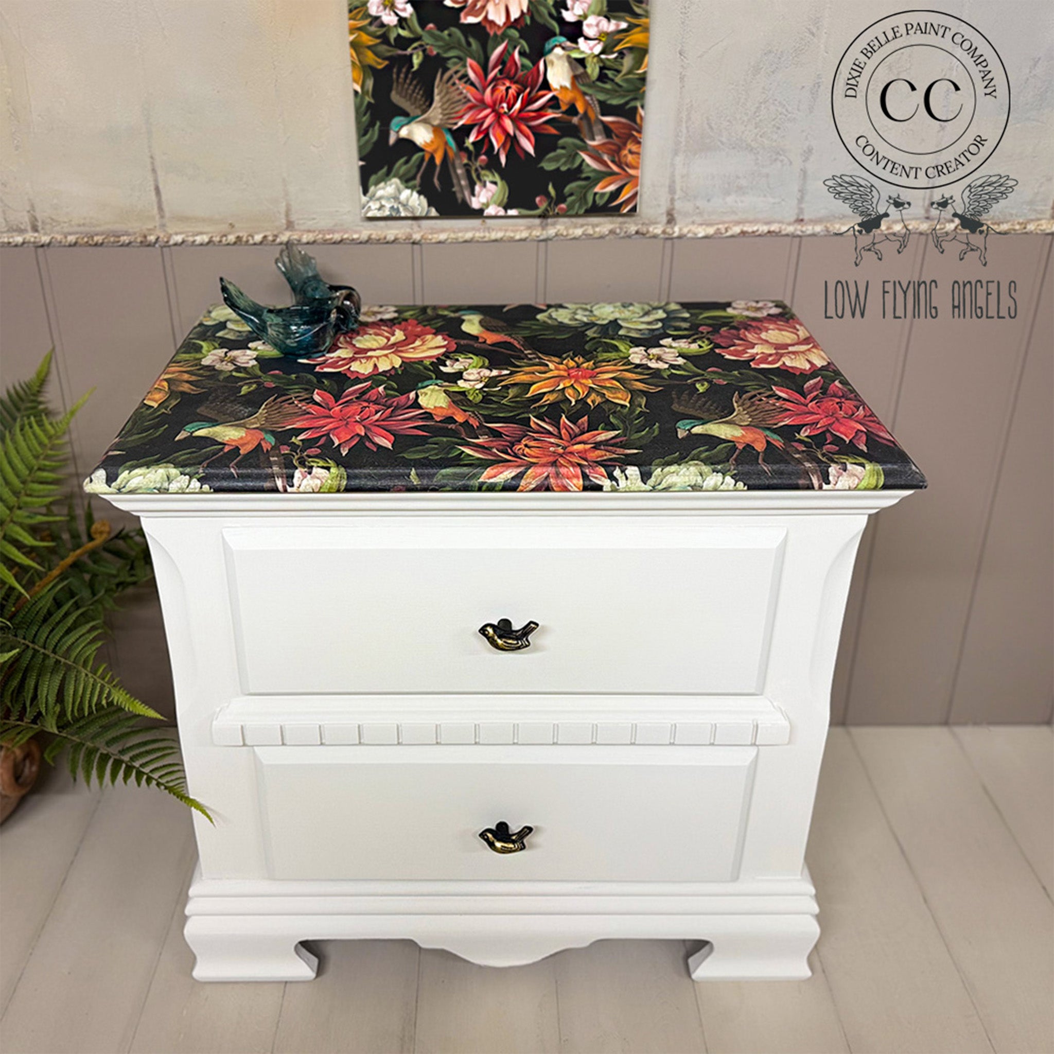 White dresser with floral patterned cover against a neutral wall.