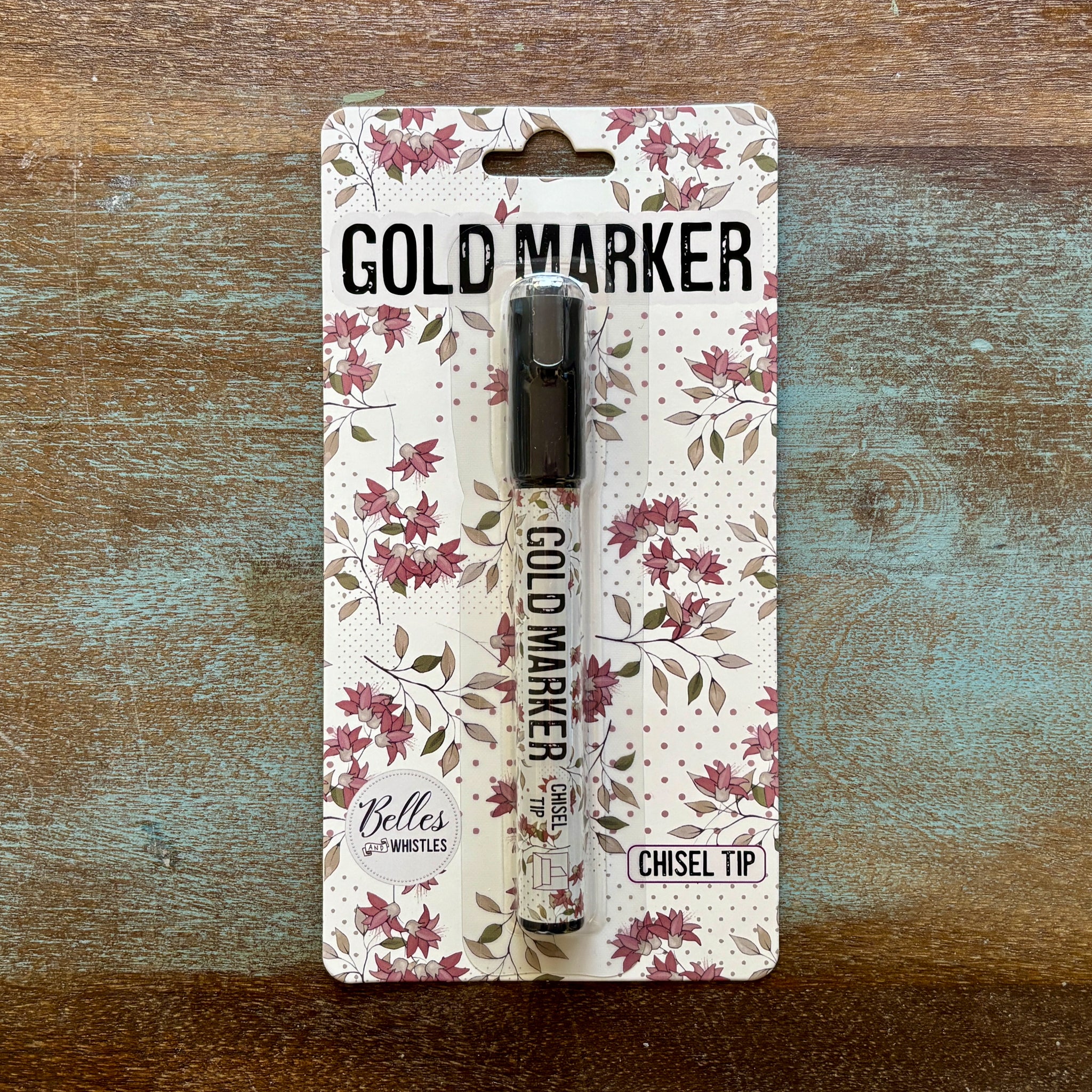 A package of Belles and Whistles' Gold Metallic Paint Marker Pen is against a wood background.