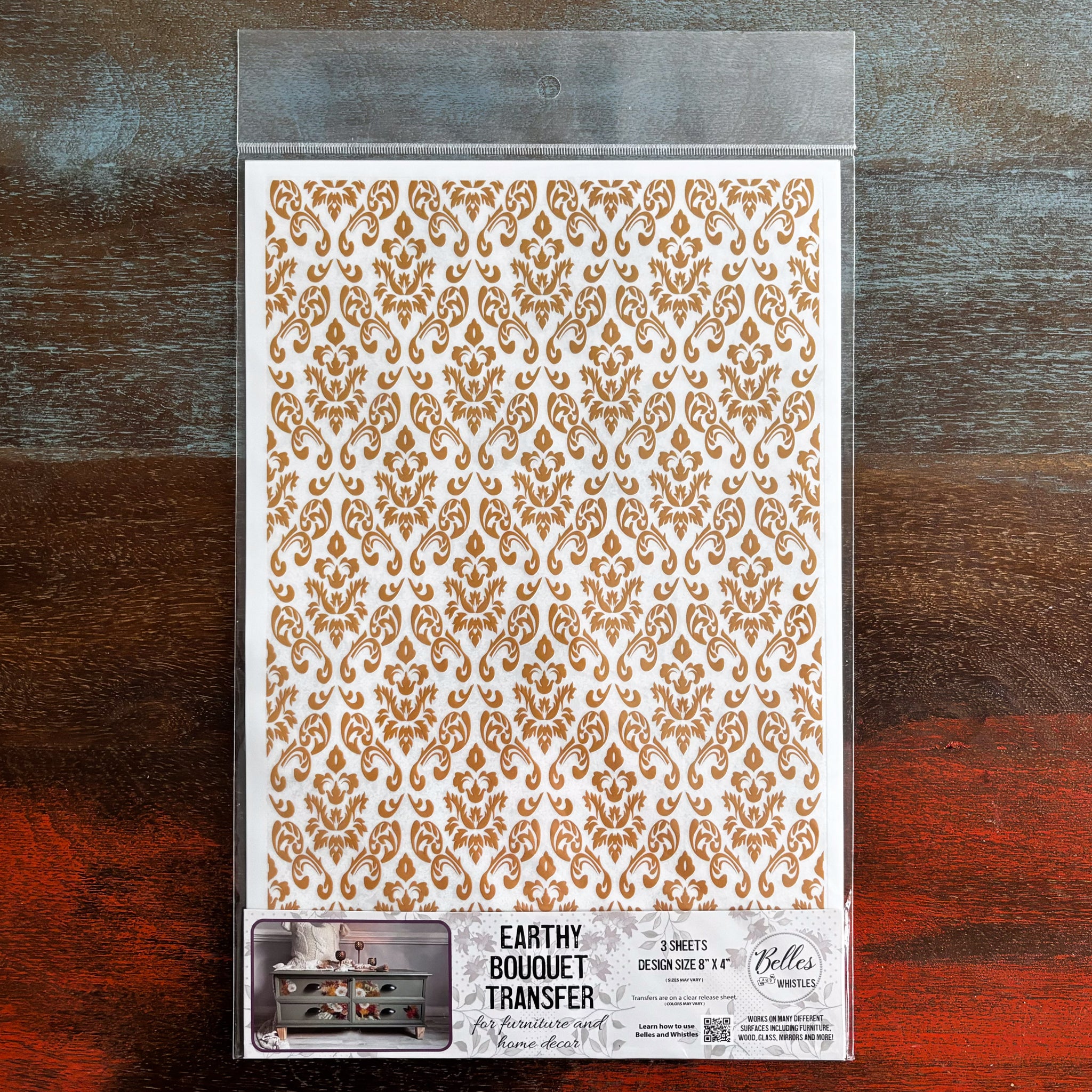 A package of Belles & Whistles’ Earthy Bouquet small transfer is against a dark wood background.