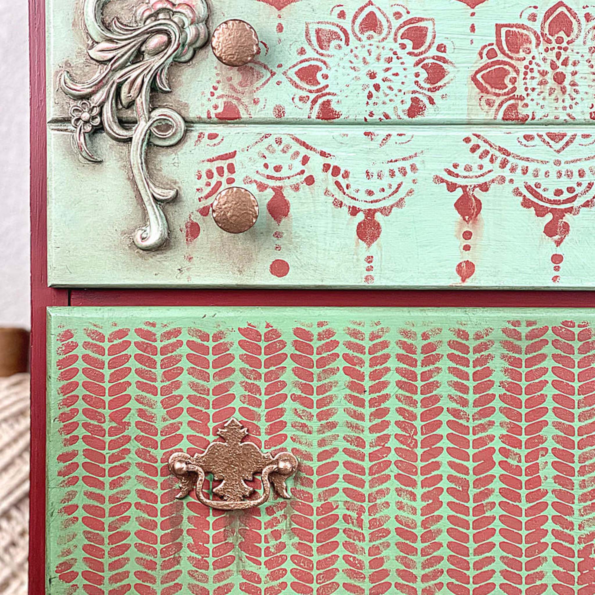 A close-up of 2 drawers are painted pale green with stencil designs in red on them. The bottom drawer features Belles & Whistles Cozy Sweater mylar stencil design on it.
