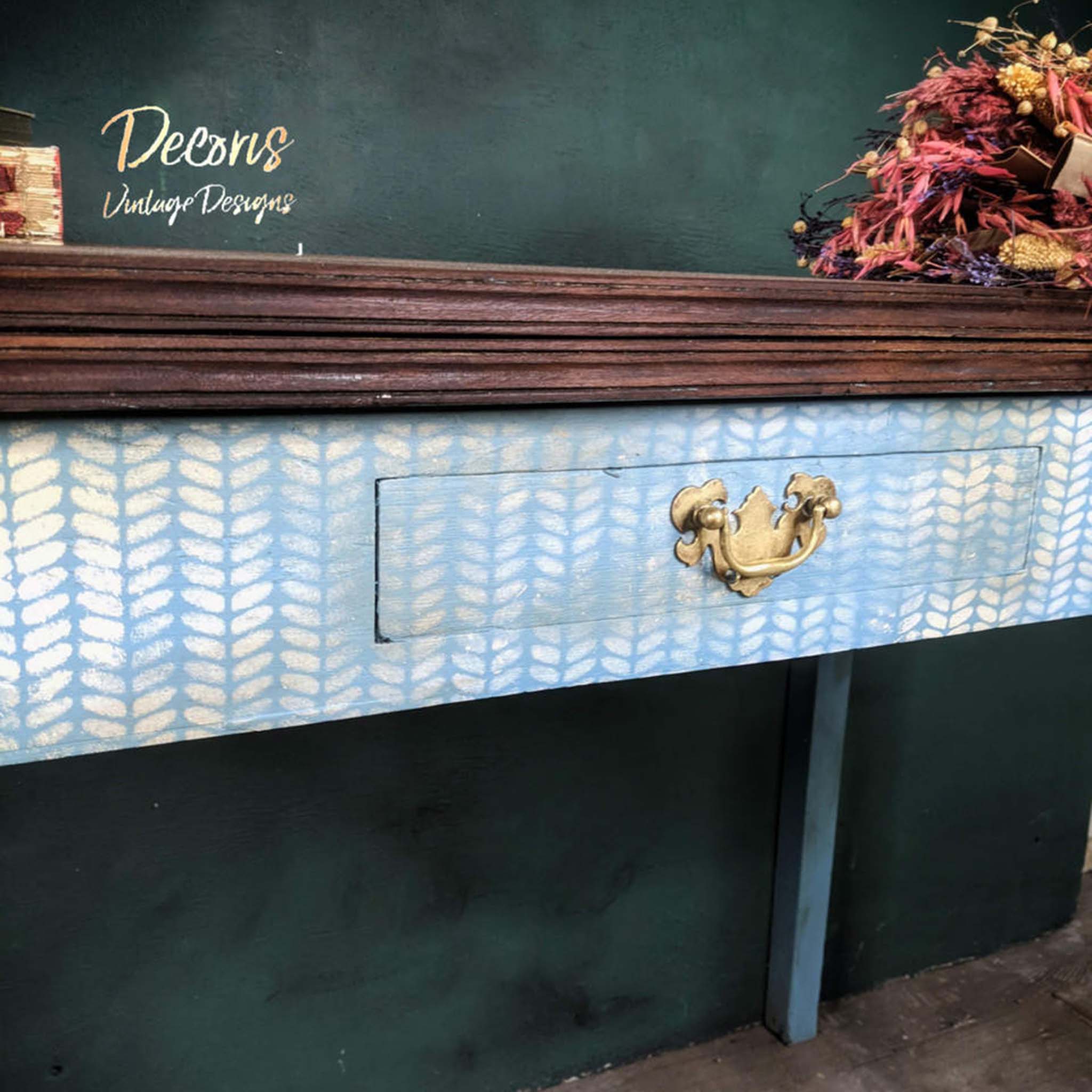 A vintage desk with a small drawer refurbished by Decoris Vintage Designs is painted light blue with a natural wood desktop. Belles & Whistles Cozy Sweater mylar stencil design is featured on the blue in a soft white color.