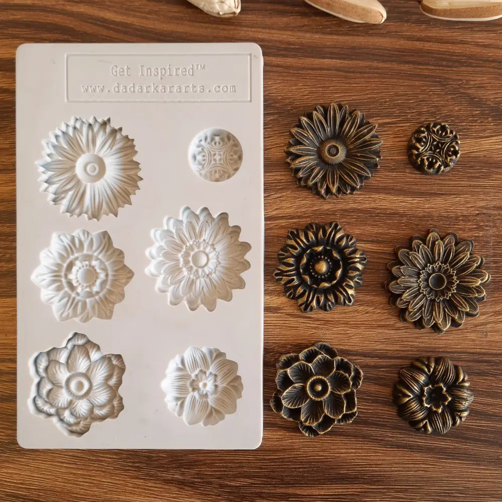 A light beige silicone mold and bronze colored castings of 6 posy flower heads are against a wood background.