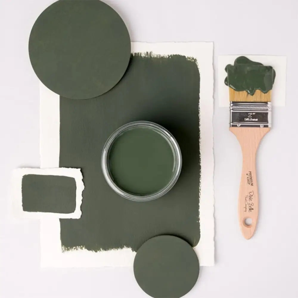 A paint brush, paper, and round wood samples of Dixie Belle's Briar Patch Chalk Mineral Paint are against a white background.